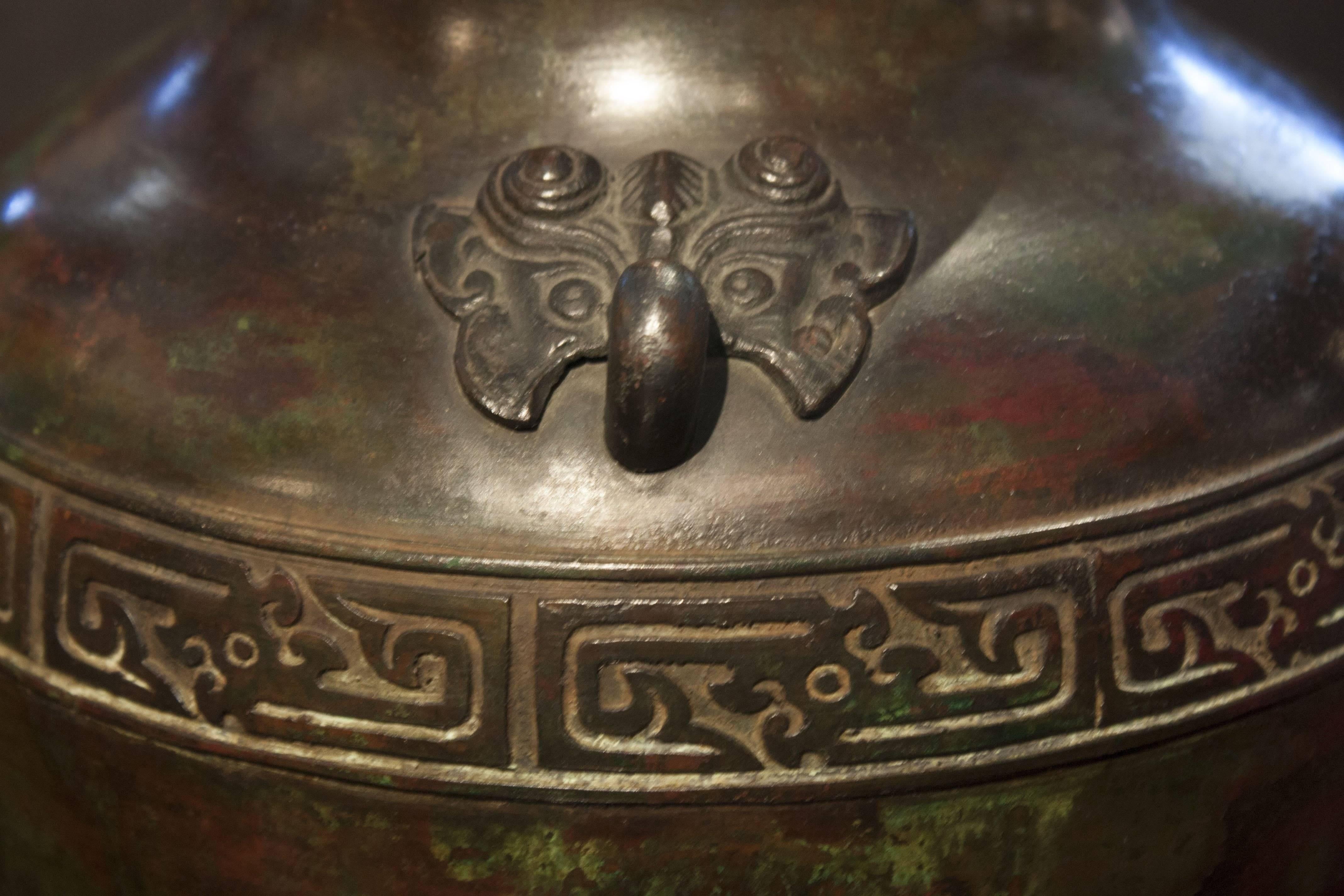 An elegant and beautifully cast early 20th century Chinese bronze vase in the archaic style with a gorgeous lacquer simulated patina in shades of brown, red and green. 
The shoulders applied with opposing taotie (ogre) mask ring handles above a