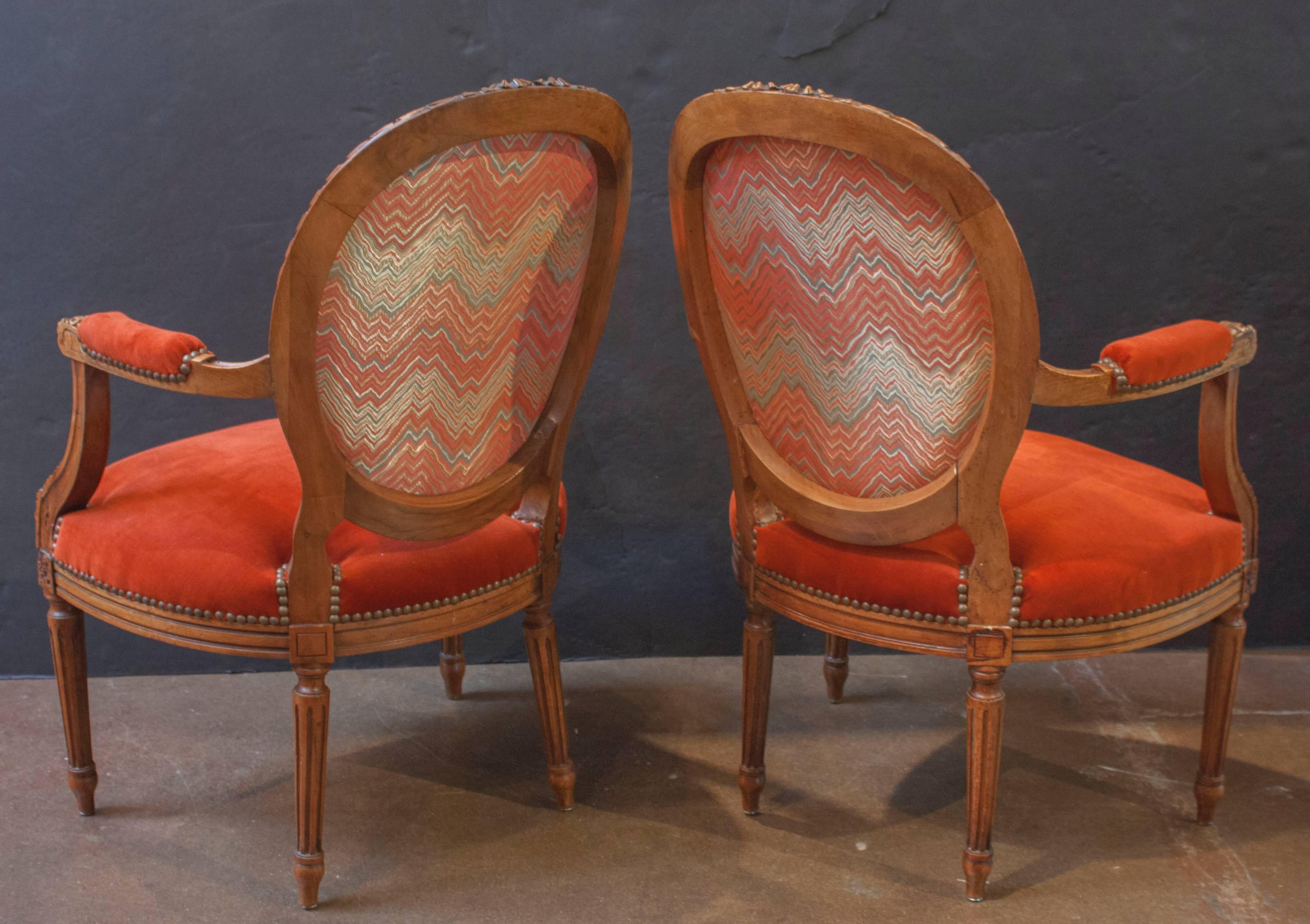 Dating to circa 1900, and carved in the Louis XVI style, this pair of charming armchairs feature the traditional medallion shaped back, giving way to graceful and sweeping open arms, a generous rounded seat, and neoclassical straight, fluted legs.