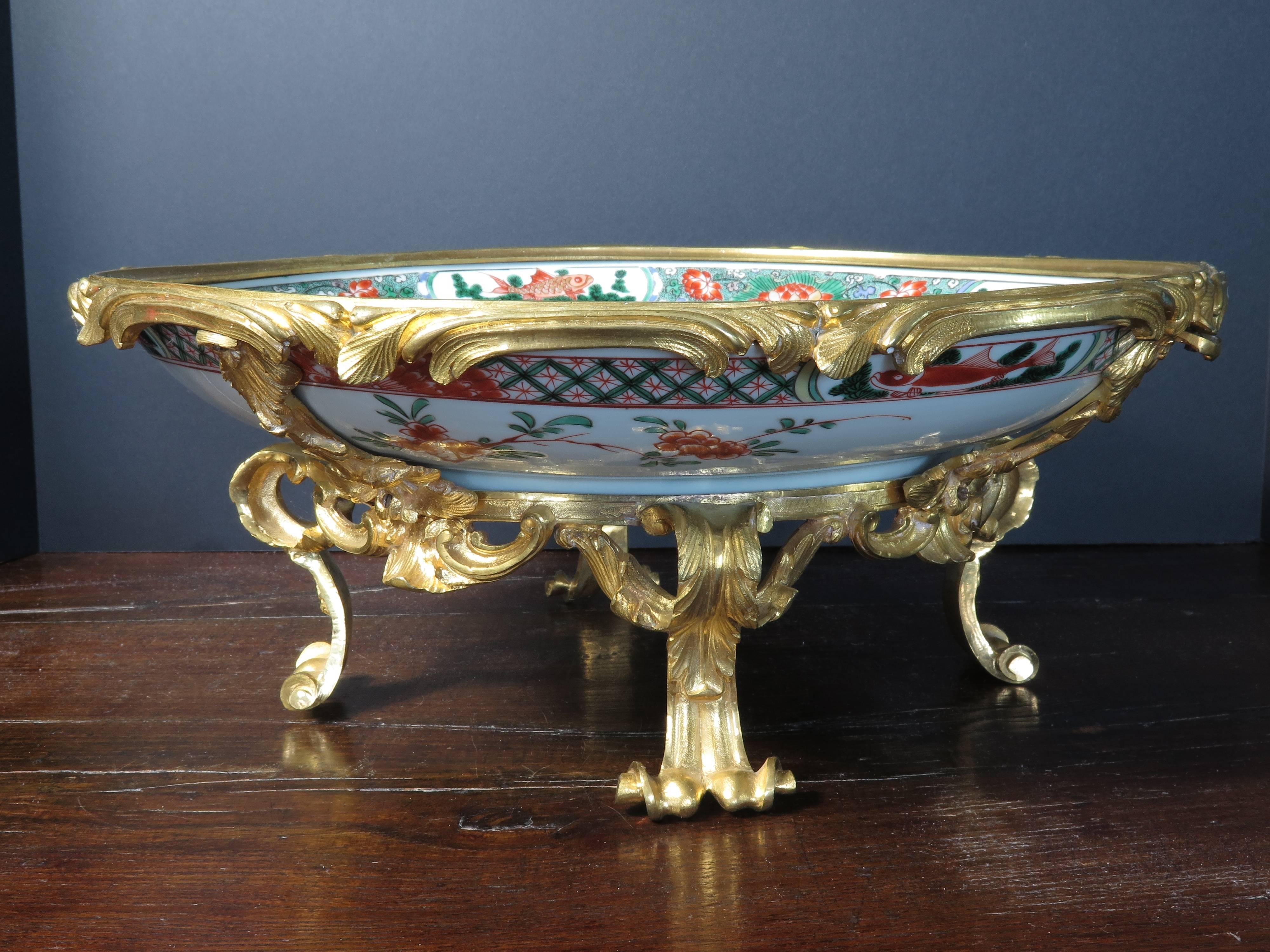 This gorgeous centerpiece has been created by the fortuitous marriage of a 17th century, Kangxi Period Famille verte enameled porcelain charger, with a set of custom 19th century French gilt bronze ormolu mounts.

The Chinese porcelain charger is