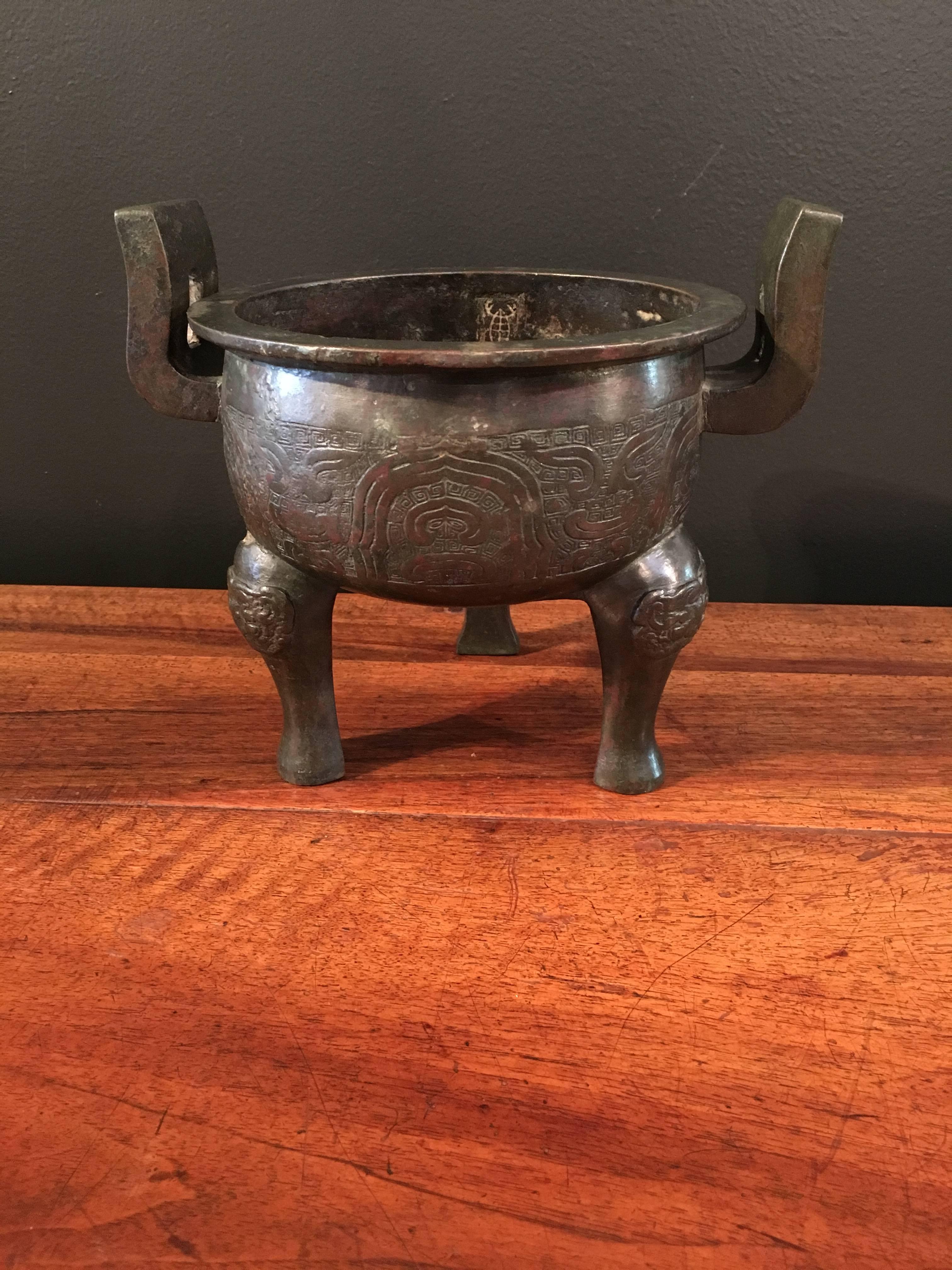 The tripod vessel is heavily cast and features animal mask legs and two large upturned handles. The scrolling archaic design of a stylized dragon upon a lewen ground.
An attractive patina of dark red, green and brown lacquer, with areas of natural