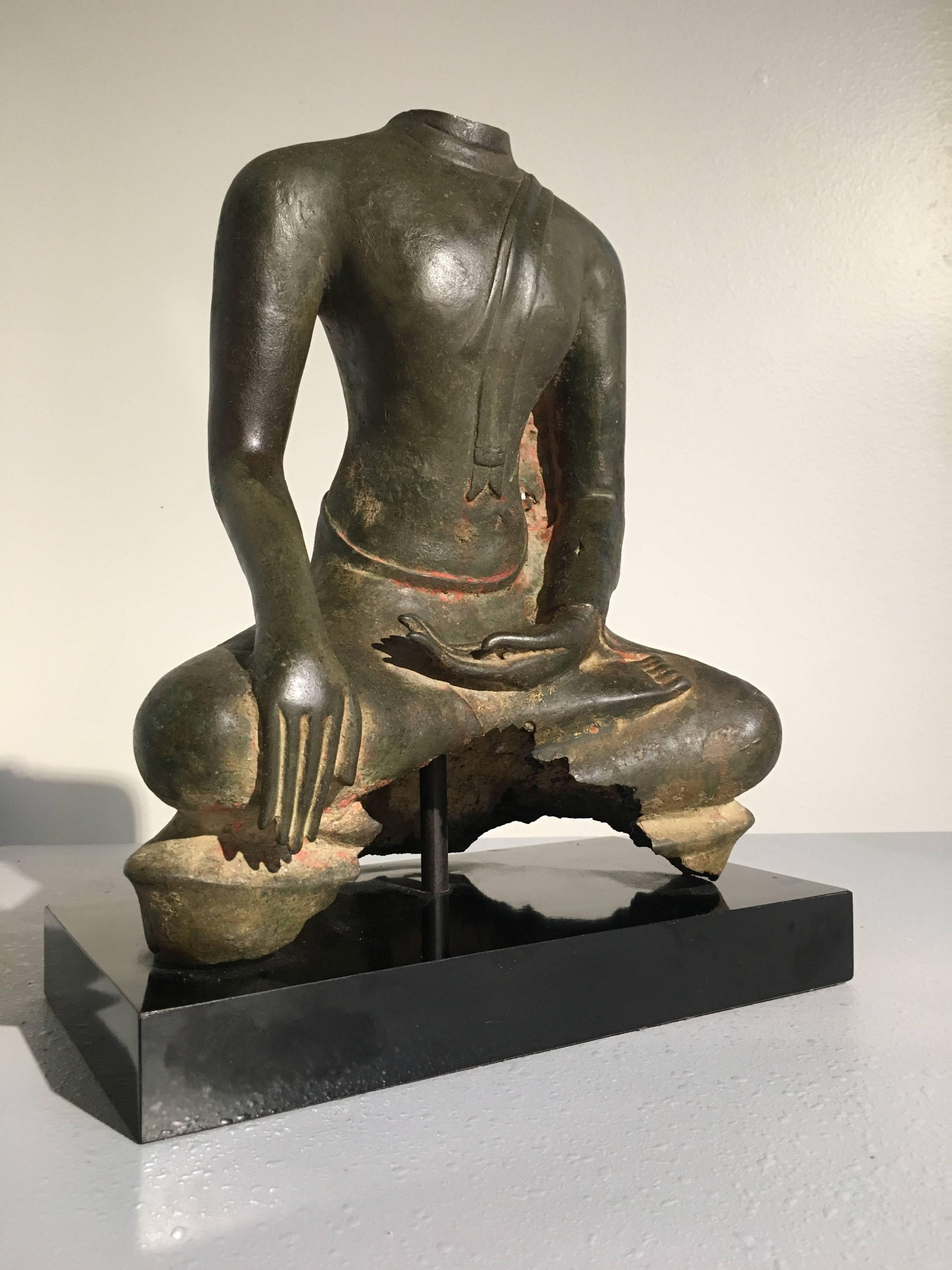 The Buddha is portrayed in a seated position with legs crossed, one hand resting upturned in his lap, the other draped gently over his knee in bhumiparsha mudra, signifying the moment of his enlightenment. He is dressed in simple robes that hug the
