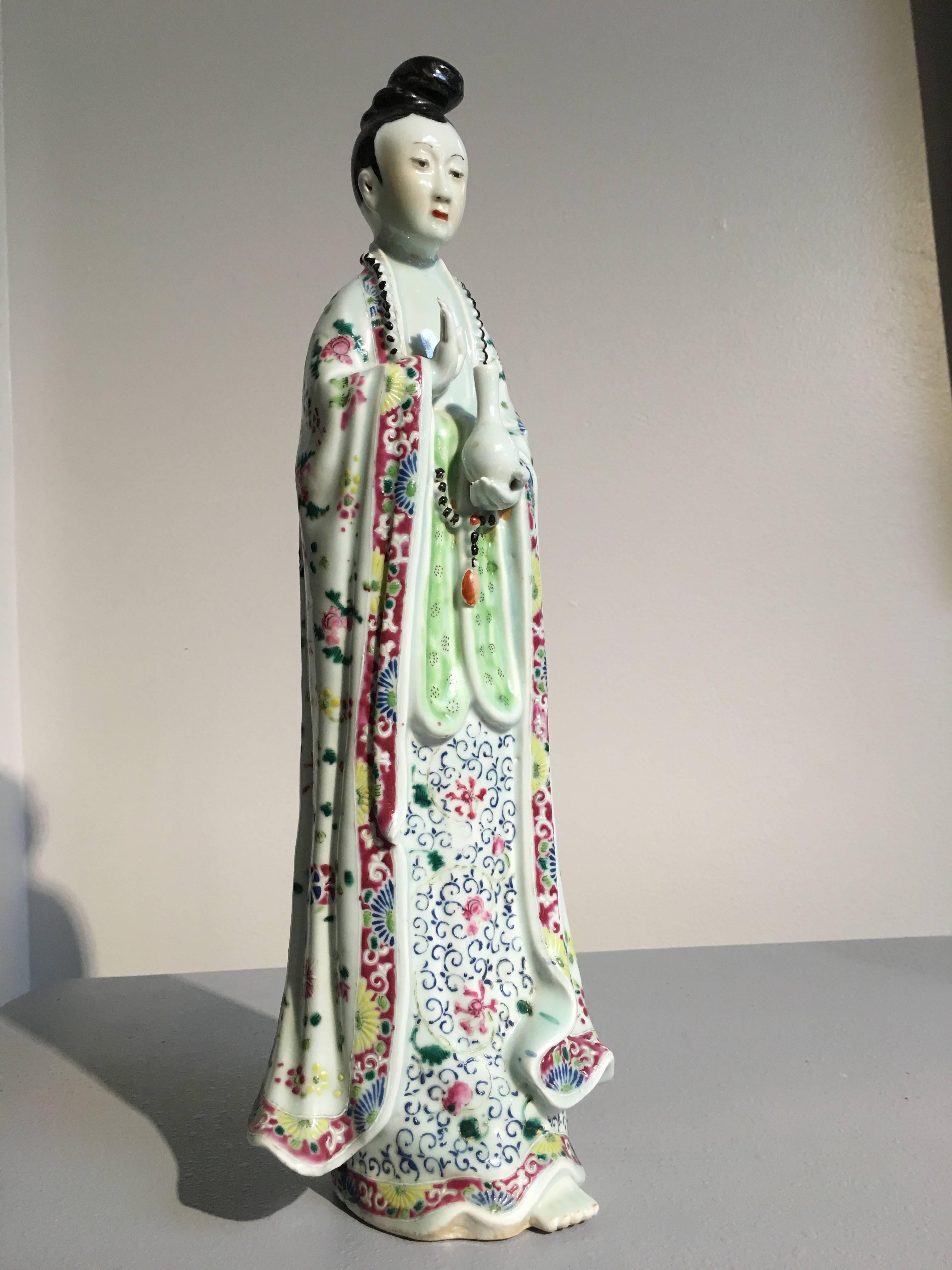 An unusually tall Chinese porcelain model of Guanyin, the goddess of mercy and compassion. She is portrayed standing, dressed in voluminous robes that billow around her, finely painted with vibrant famille rose enamels. Her attribute, the sacred