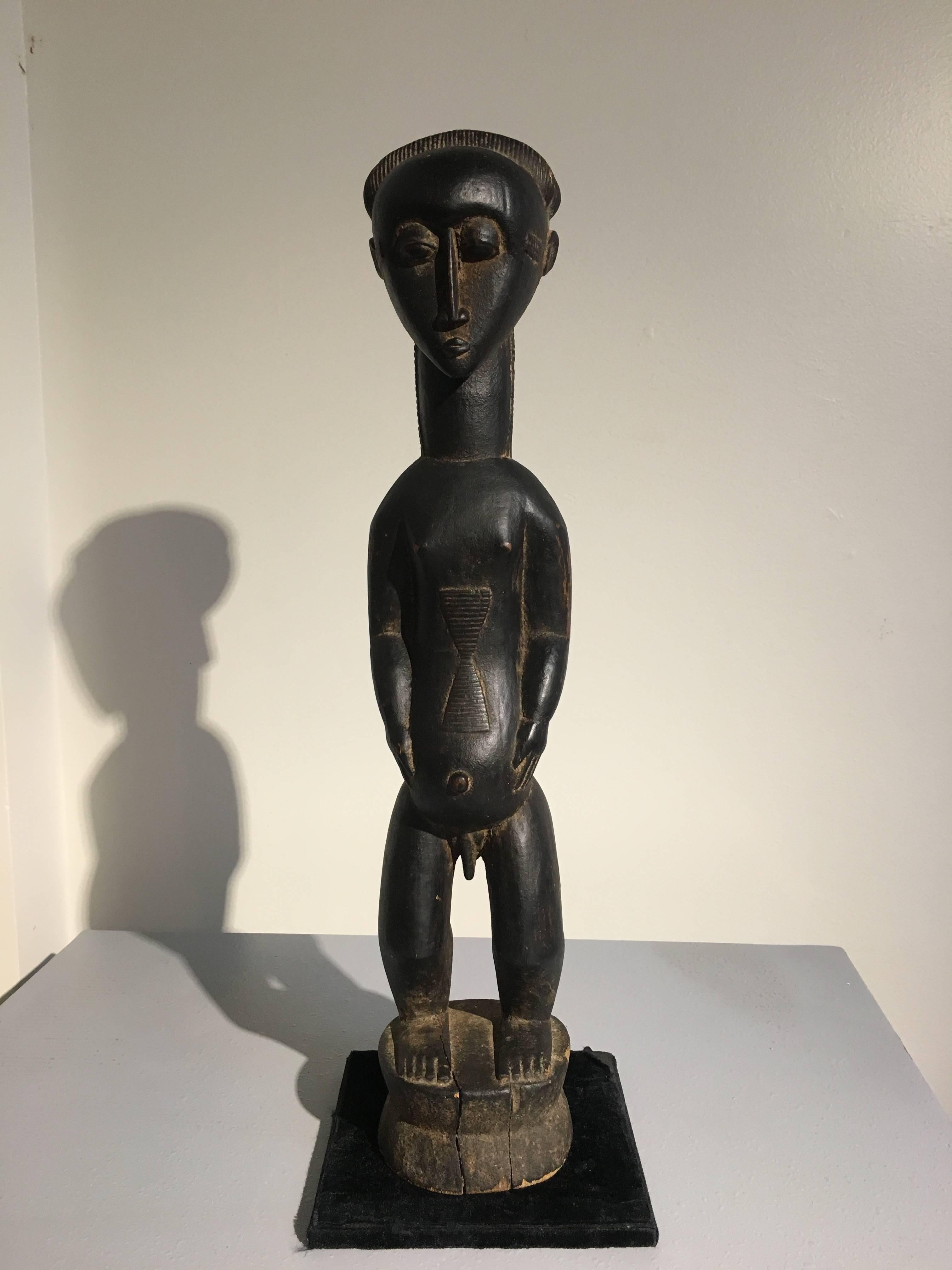 A superbly carved Baule or Djmini male figure. Seemingly produced by a master tribal carver for the European market during the early part of the 20th century. 
Of traditional form, the young male figure is portrayed standing upon short, squat legs,