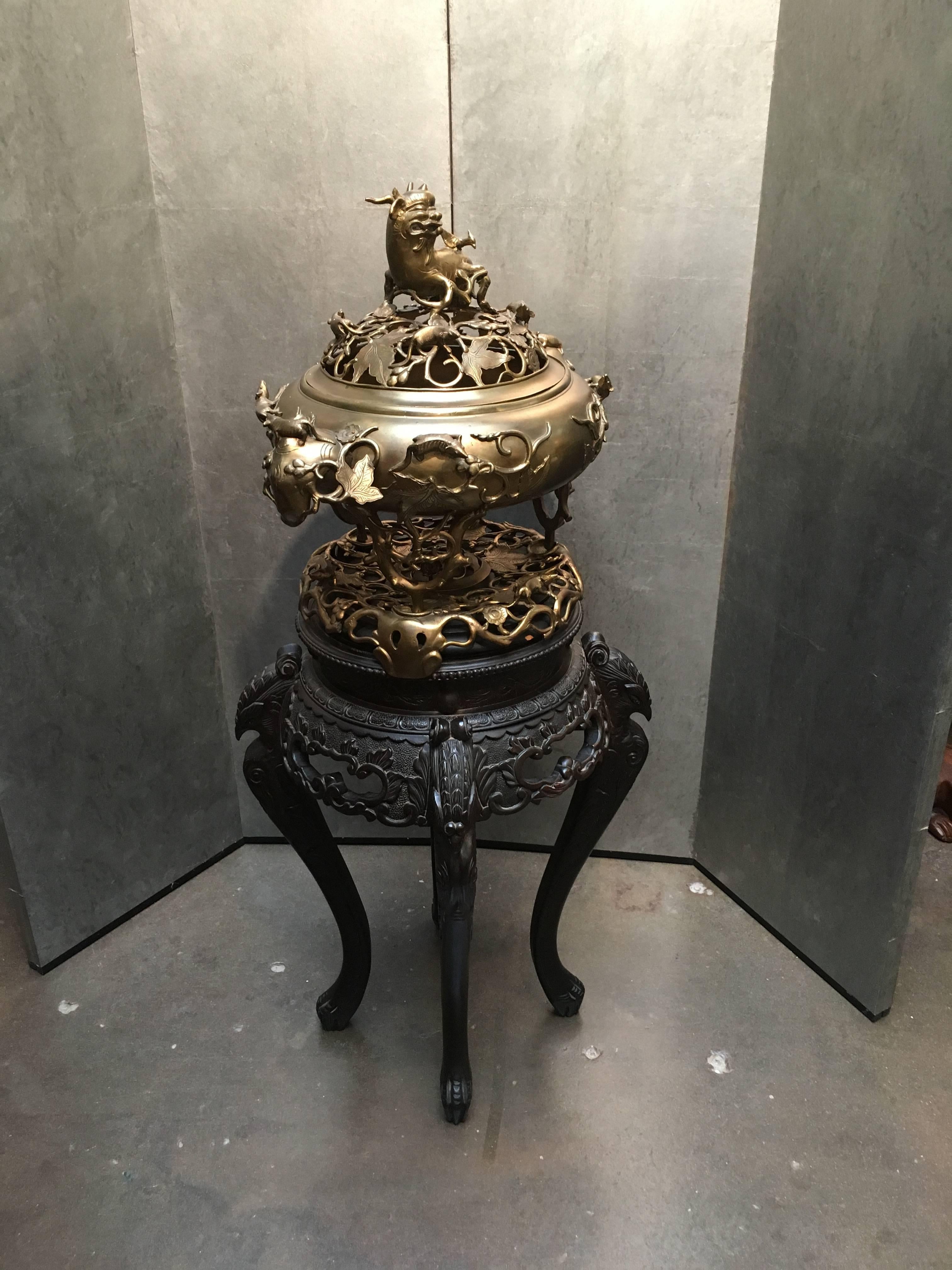 A large and impressive mid-20th century Chinese brass censer, stand and cover on a customized 19th century Japanese export Meiji period carved and ebonized wood stand.
The tripod censer sits on an associated base. The legs formed as scrolled grape