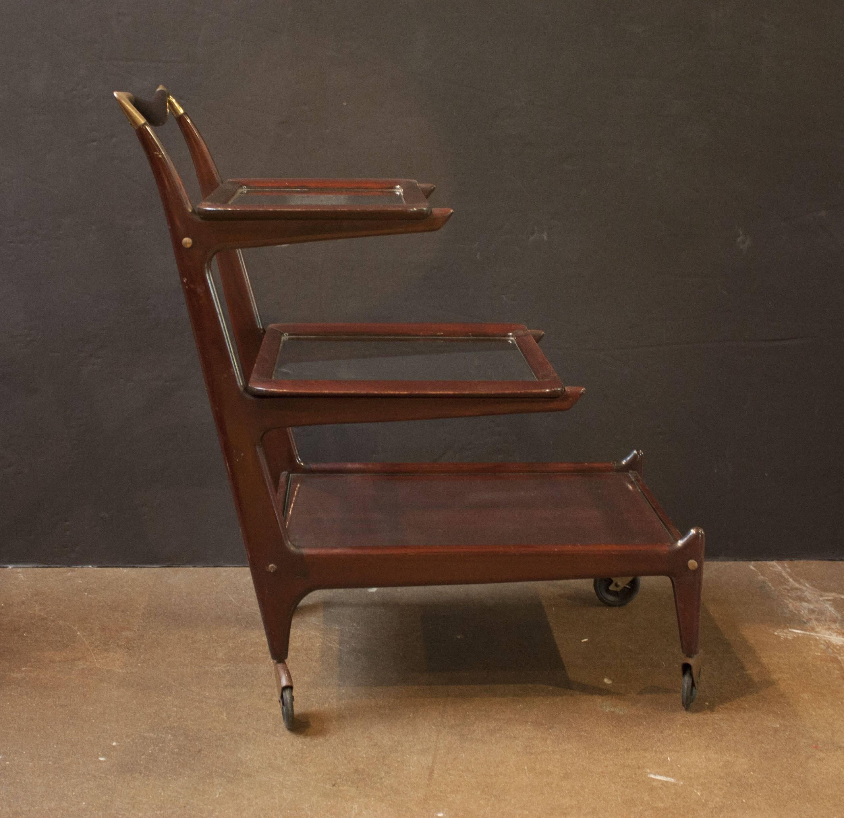 An Italian, Mid-Century three-tiered rosewood bar cart with two removable serving trays by Cesare Lacca for Cassina. 
The cart sits on four wheels, and is made of a deep reddish brown rosewood, with hints of purple, finished with a French polish.