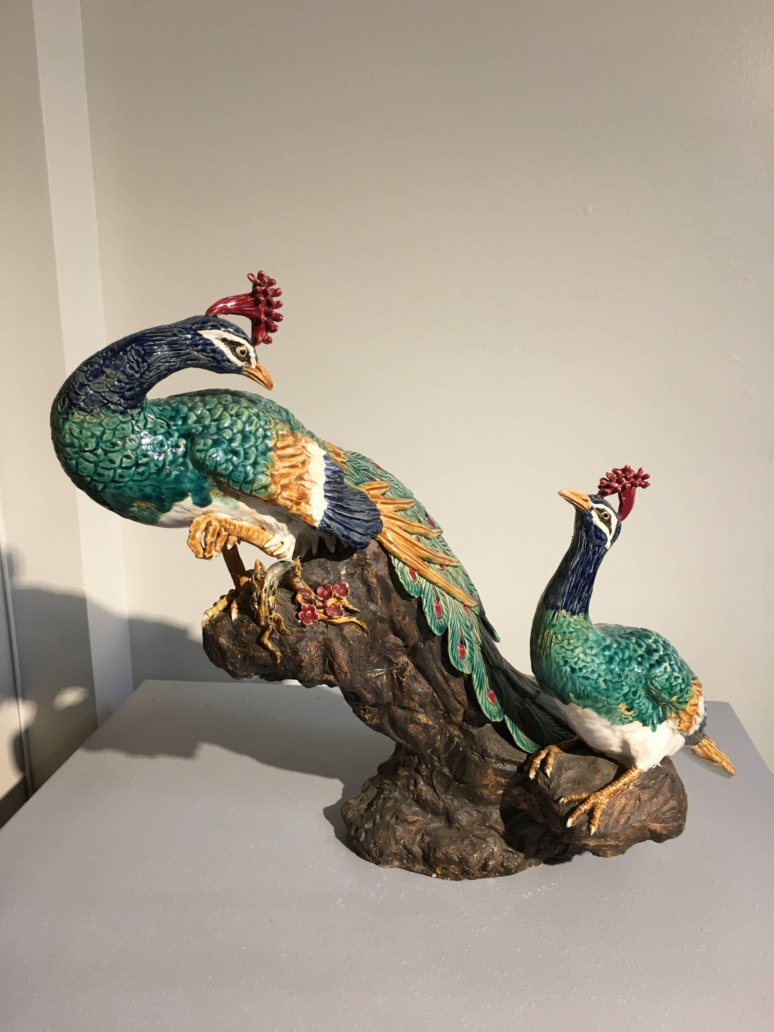 A large sculpture of a peacock and peahen perched on a rocky outcrop.
Well molded, and brilliantly glazed with green, blue, yellow, white and red. The peacock is perched on higher ground, his magnificent tail trailing out behind him, head turned to