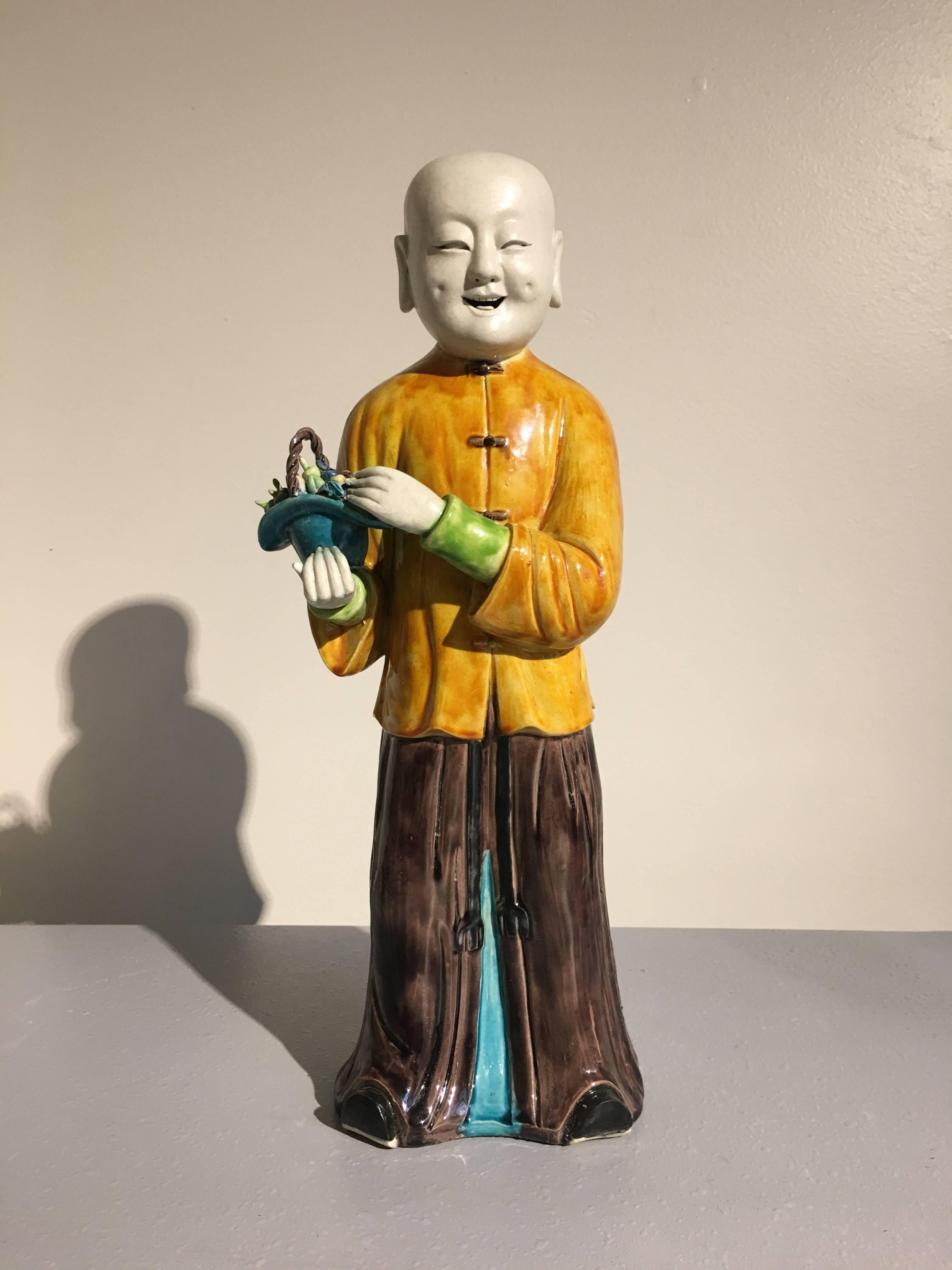 A large porcelain model of a boy, possibly the Taoist immortal Lan Caihe, Republic Period, early 20th century, China. 

The figure is portrayed standing, dressed in aubergine glazed robes, wearing a mustard glazed surcoat, and holding a turquoise