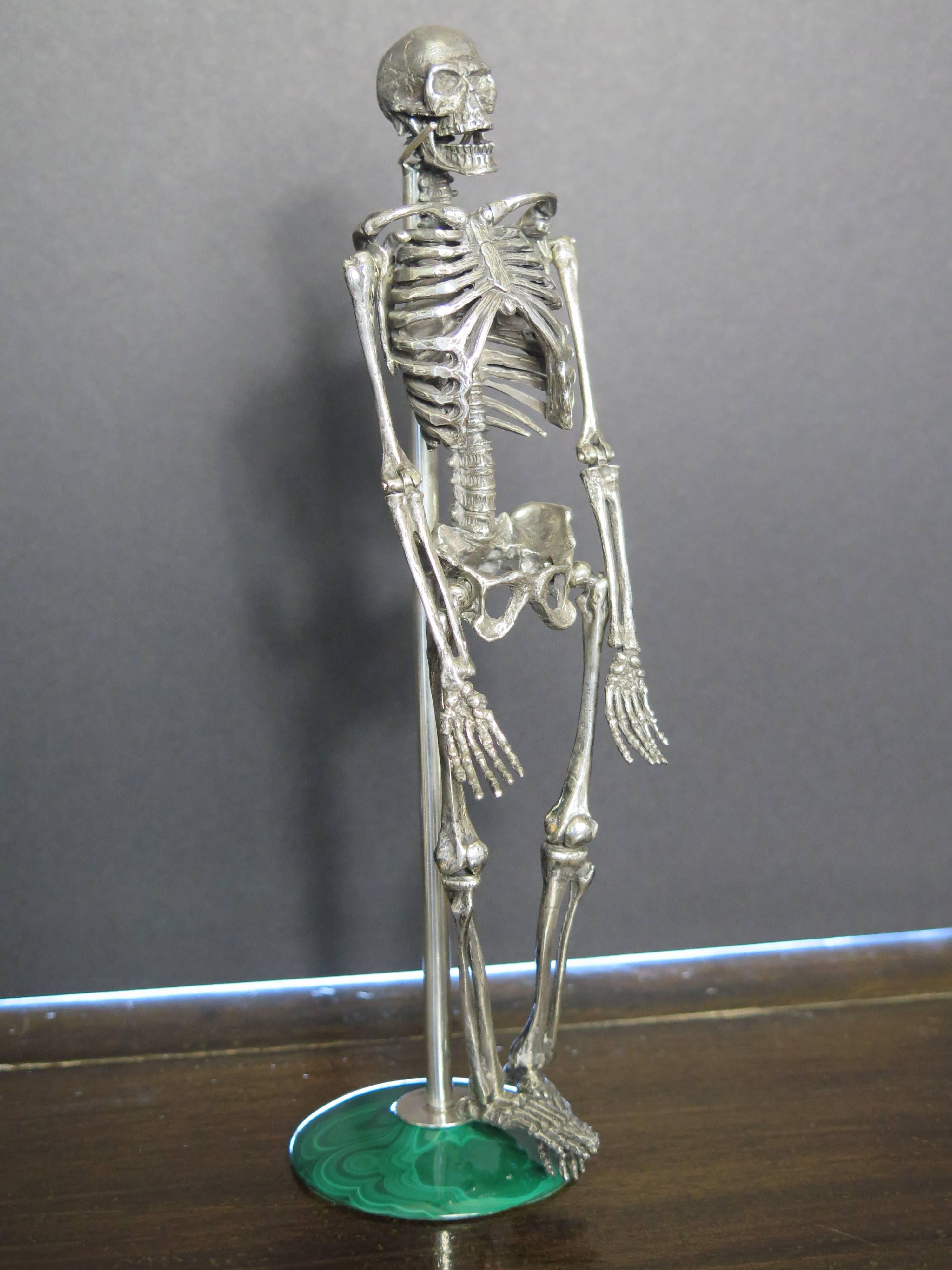 A whimsical anatomically correct silver model of a human skeleton. Its jaw, arms and legs can be placed in several positions. Italian silver. Marked. 
It comes with a malachite base metal stand. 9.5:" tall with stand. 9" without stand.