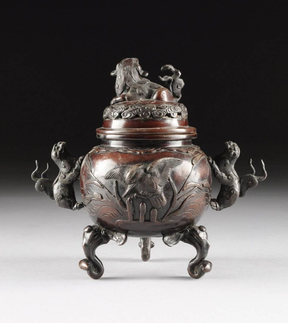 A Japanese Meiji period patinated bronze censor of globular form flanked by applied wave tailed Buddhistic lion handles beneath a collar of stylized ruyi in shallow relief, surmounted by a reticulated domed lid enclosing stylized scrolling clouds