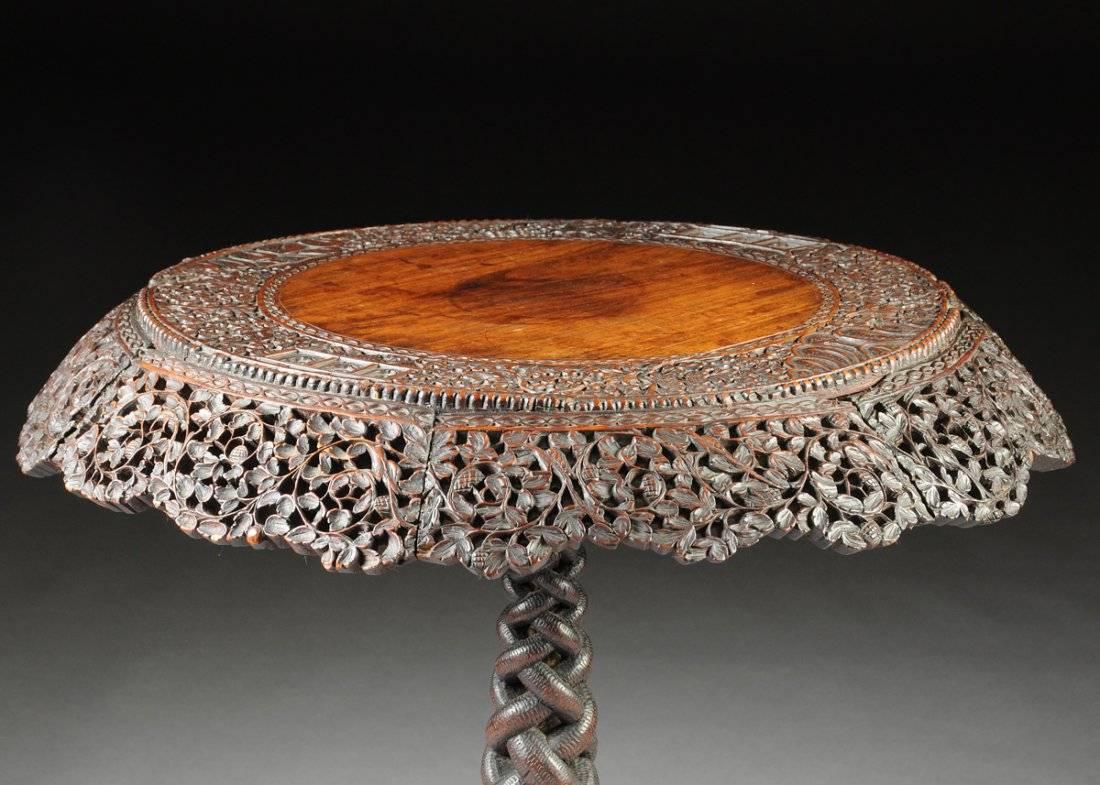 A fine and intricately carved Anglo Indian hardwood tilt top pedestal table, British Colonial period, mid 19th century, Ceylon or India.

The pedestal tilt top table features a wide circular table top carved in deep relief with a dense pictorial