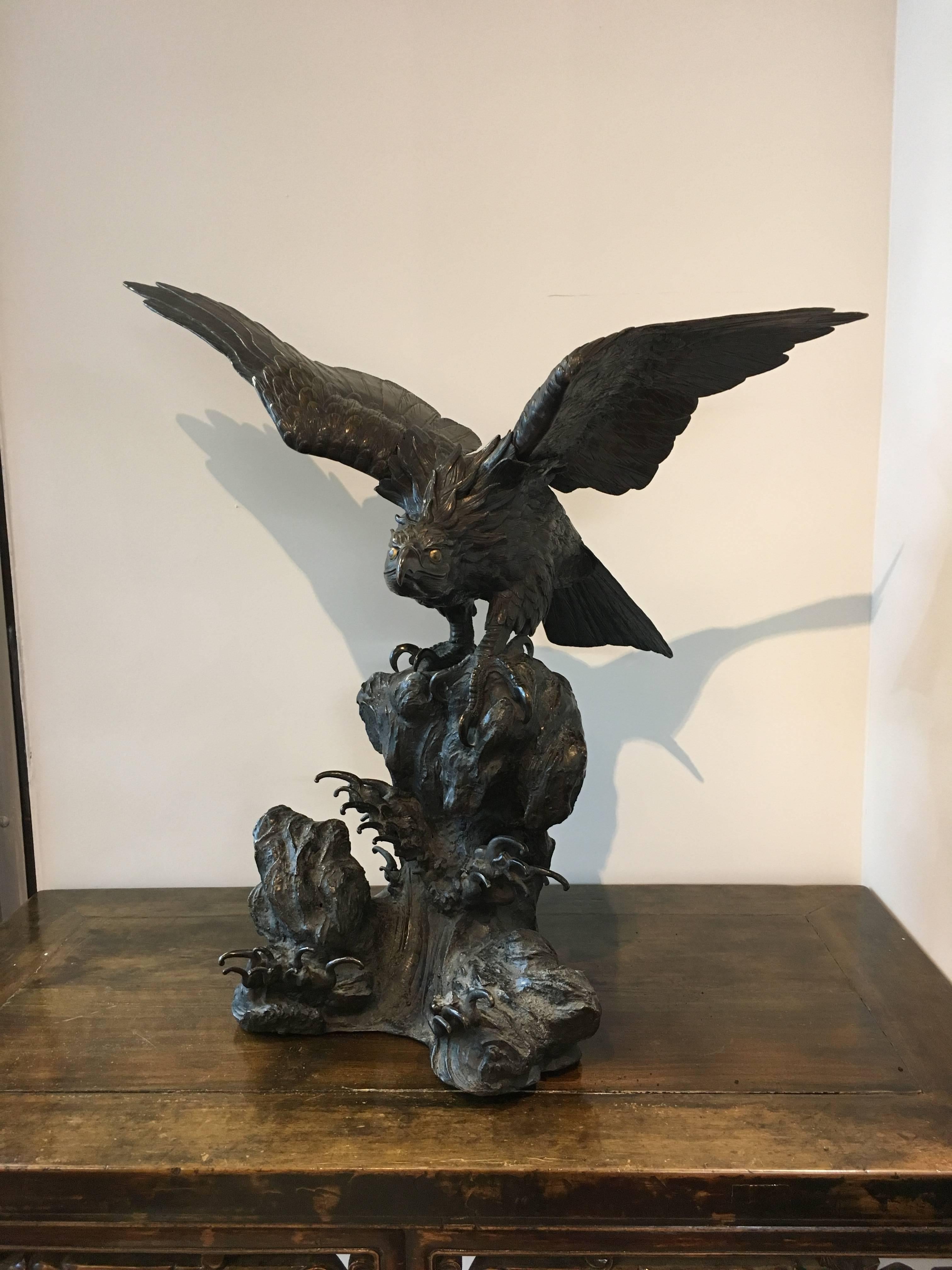 A large and powerful Japanese cast bronze model of an eagle.
The raptor is portrayed perched on a rocky outcrop, with waves crashing beneath. The bird of prey crouched down with wings outstretched, about to take off. Head down, an intense look in