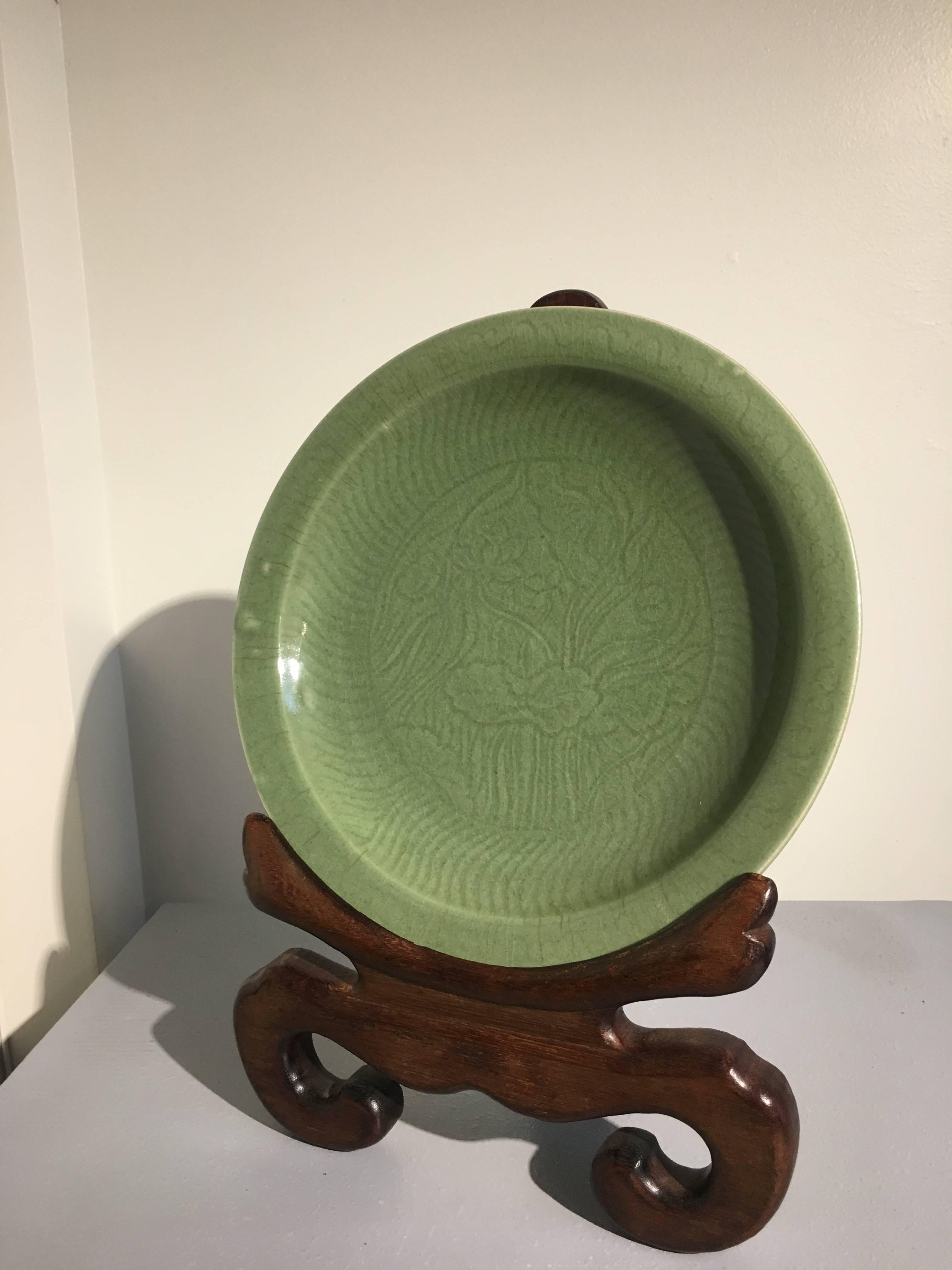 A sublime Chinese celadon glazed shallow dish or charger, Qing Dynasty, mid 18th century, China.
Beautifully glazed, with a carved decoration of a group of lotus, leaves, stalks and blossoms. The interior wall with radiating S-shaped lines, a motif