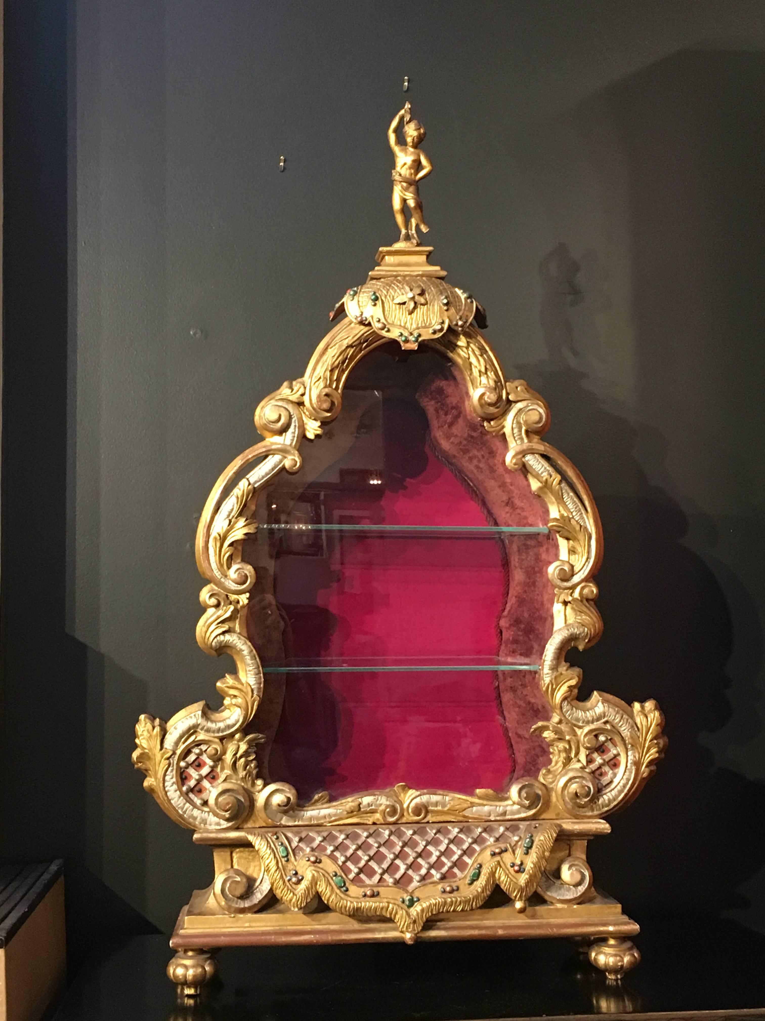 An elegant late 19th century Baroque style tabletop vitrine. The vitrine marvelously carved and richly gilt in the Baroque manner, with beautiful foliate scrollwork and polychrome detailing reminiscent of grotto architecture, all topped by a