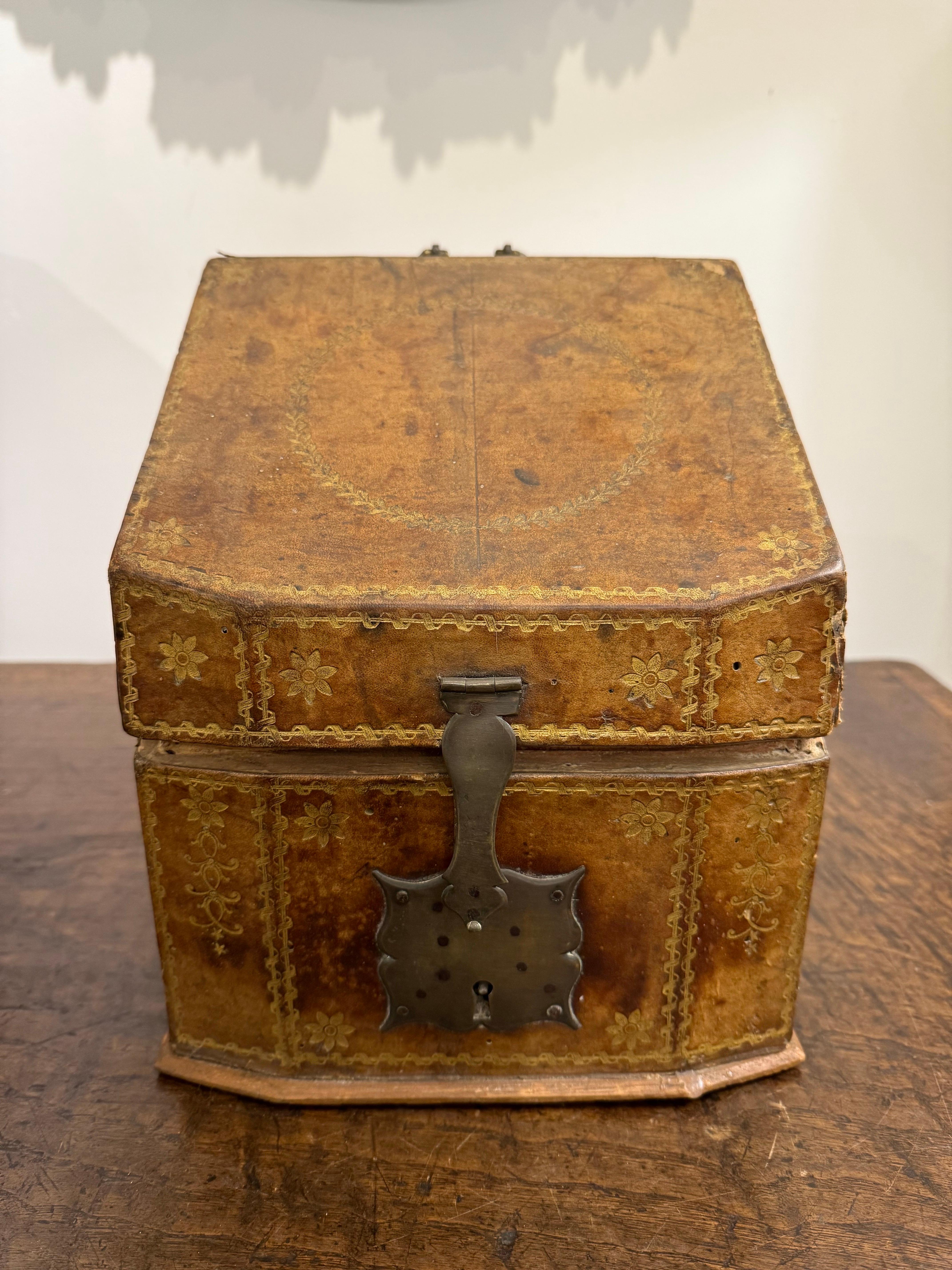 An Italian Gold Embossed Leather Knife Box, 18th Century

Description:
The wooden surface with leather overlay and painted gilt surface decoration consisting of florets and a central foliate wreath on the slope lid, with a brass handle and latch to