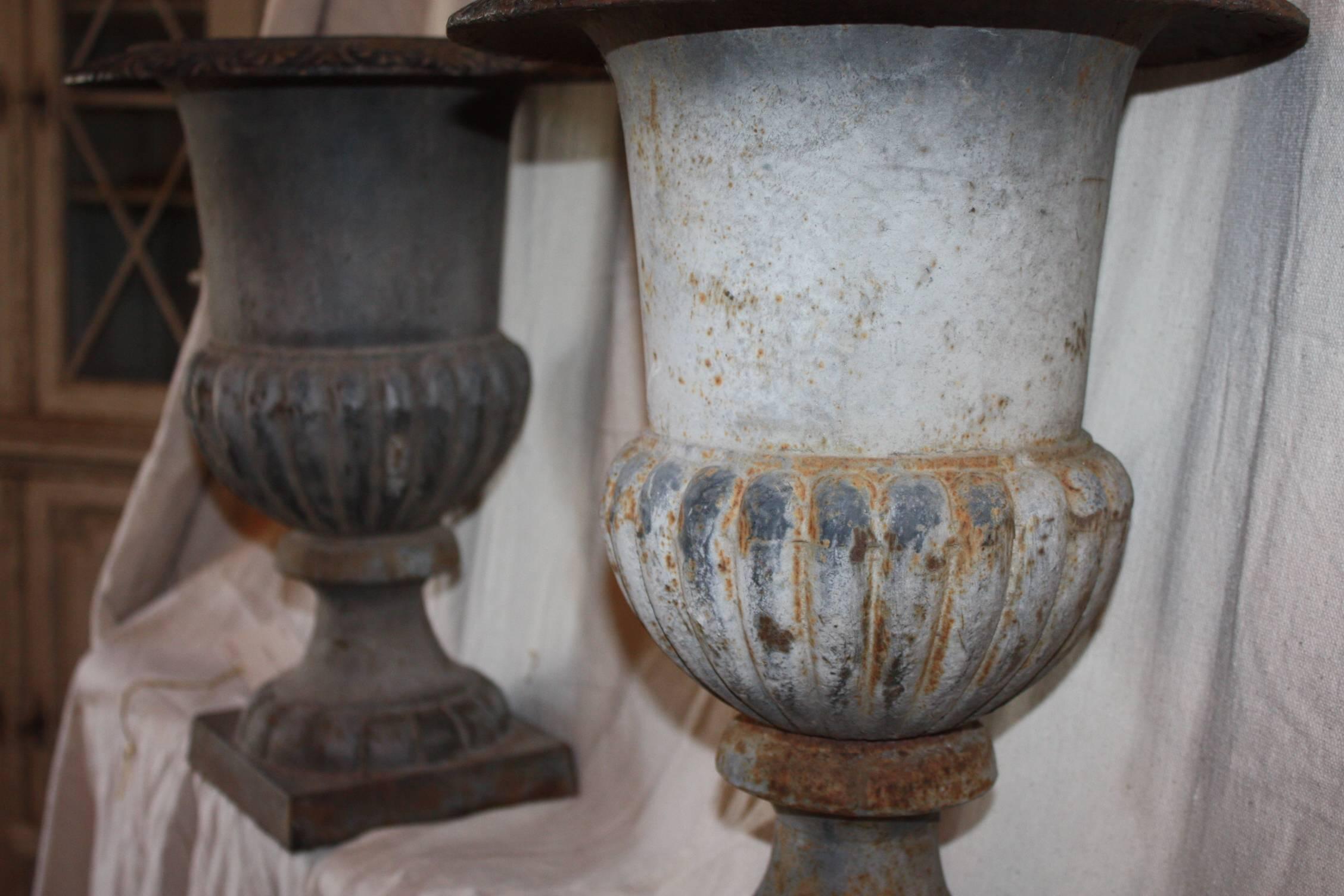 Pair of beautiful cast iron urns on pedestal bases with weathered patina finish. These would be great indoors on a mantel or as center peaces and could also be used outdoors as planters.