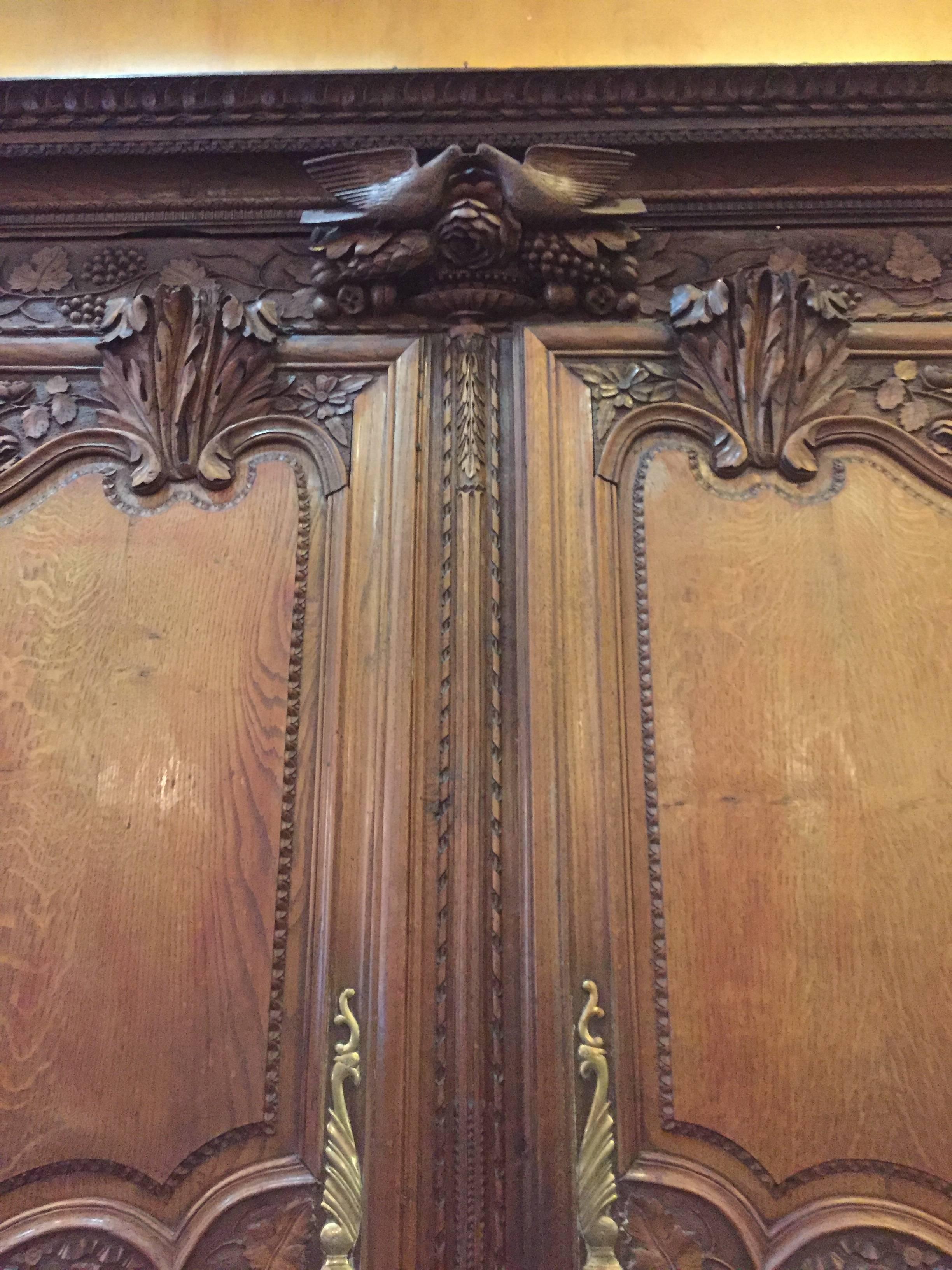 An early 19th century oak wedding armoire from Normandy, France featuring delicate carvings such as an exceptional pair of lovebirds on the top crest. The armoire opens to reveal three shelves and two locking drawers for storage.