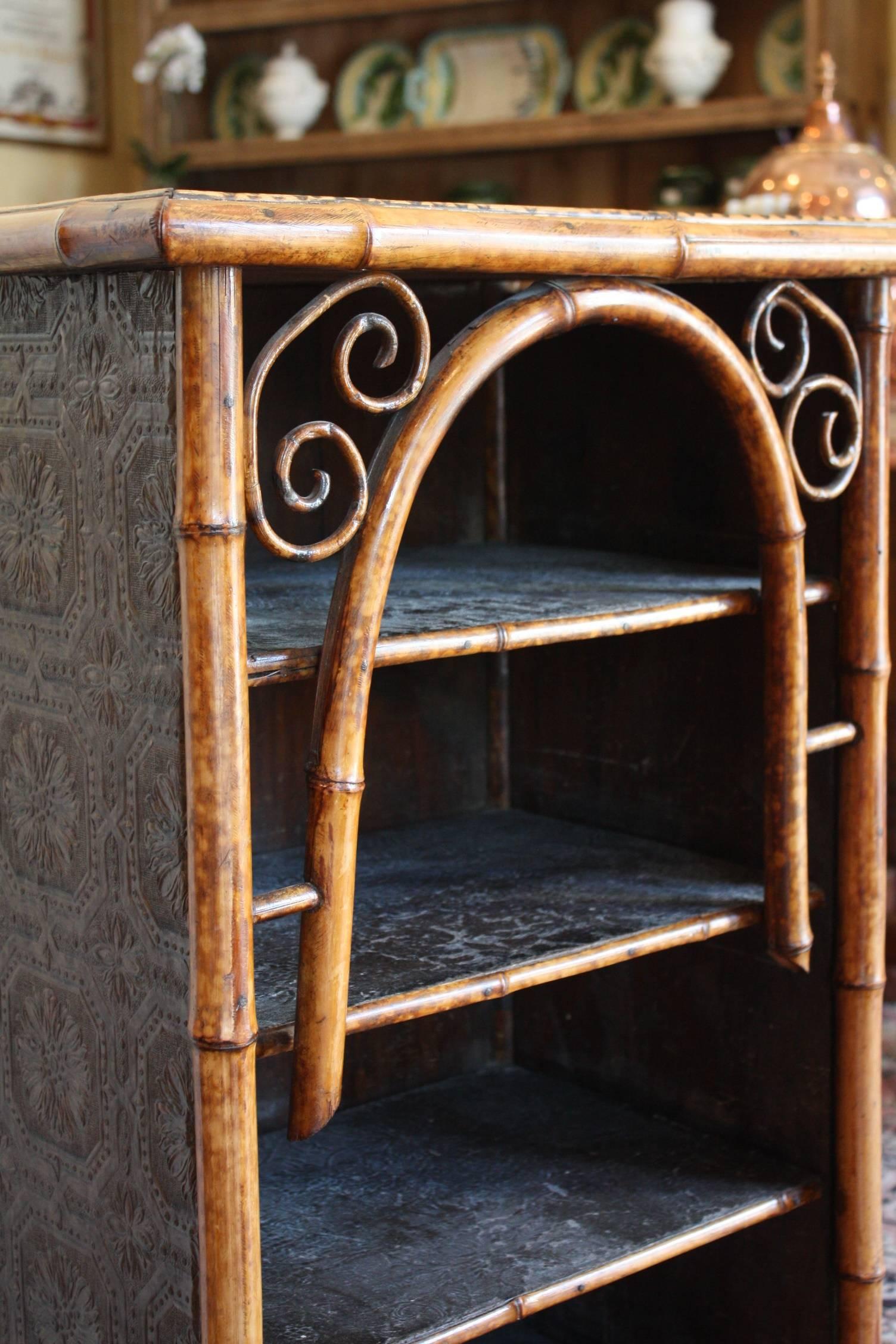 English bamboo bookcase featuring bent bamboo accents and lacquered panel and three bamboo-edged shelves, each lined with pressed paper and resting on bamboo legs.