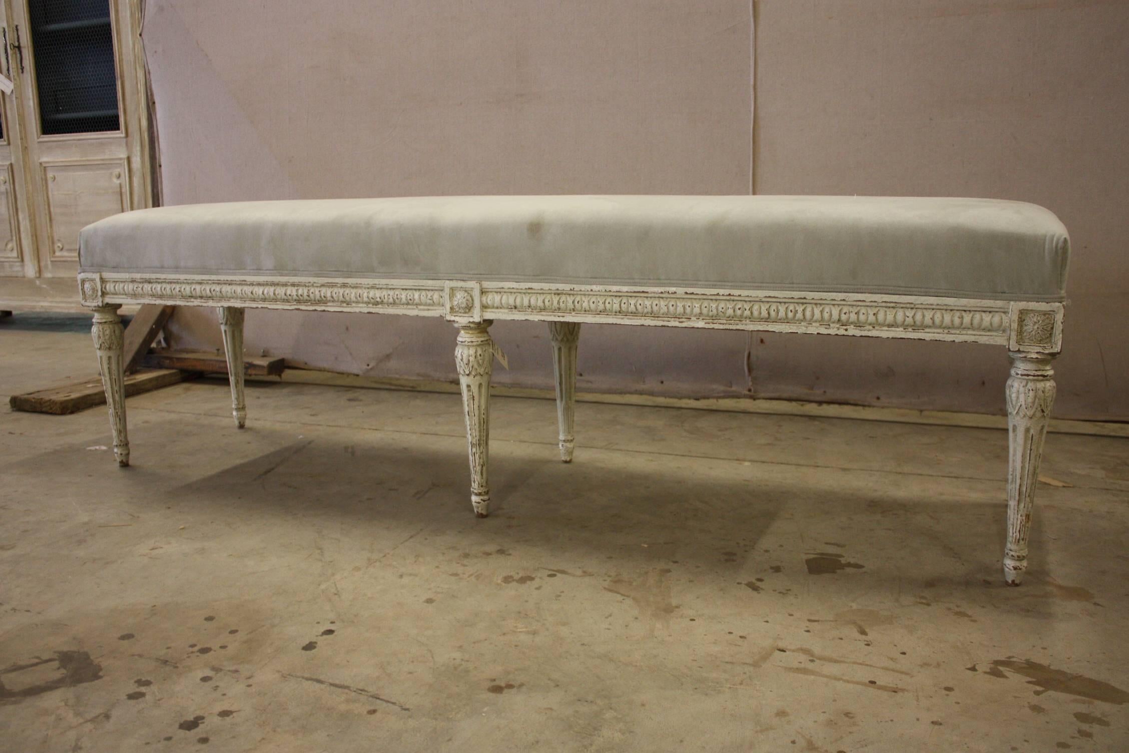 Louis XVI bench from France. Carved, circa 1880, the antique bench has six tapered legs, symmetrical carvings around the apron, and is reupholstered with a thick grey suede. Due to its size and narrow profile, the bench would also make the perfect