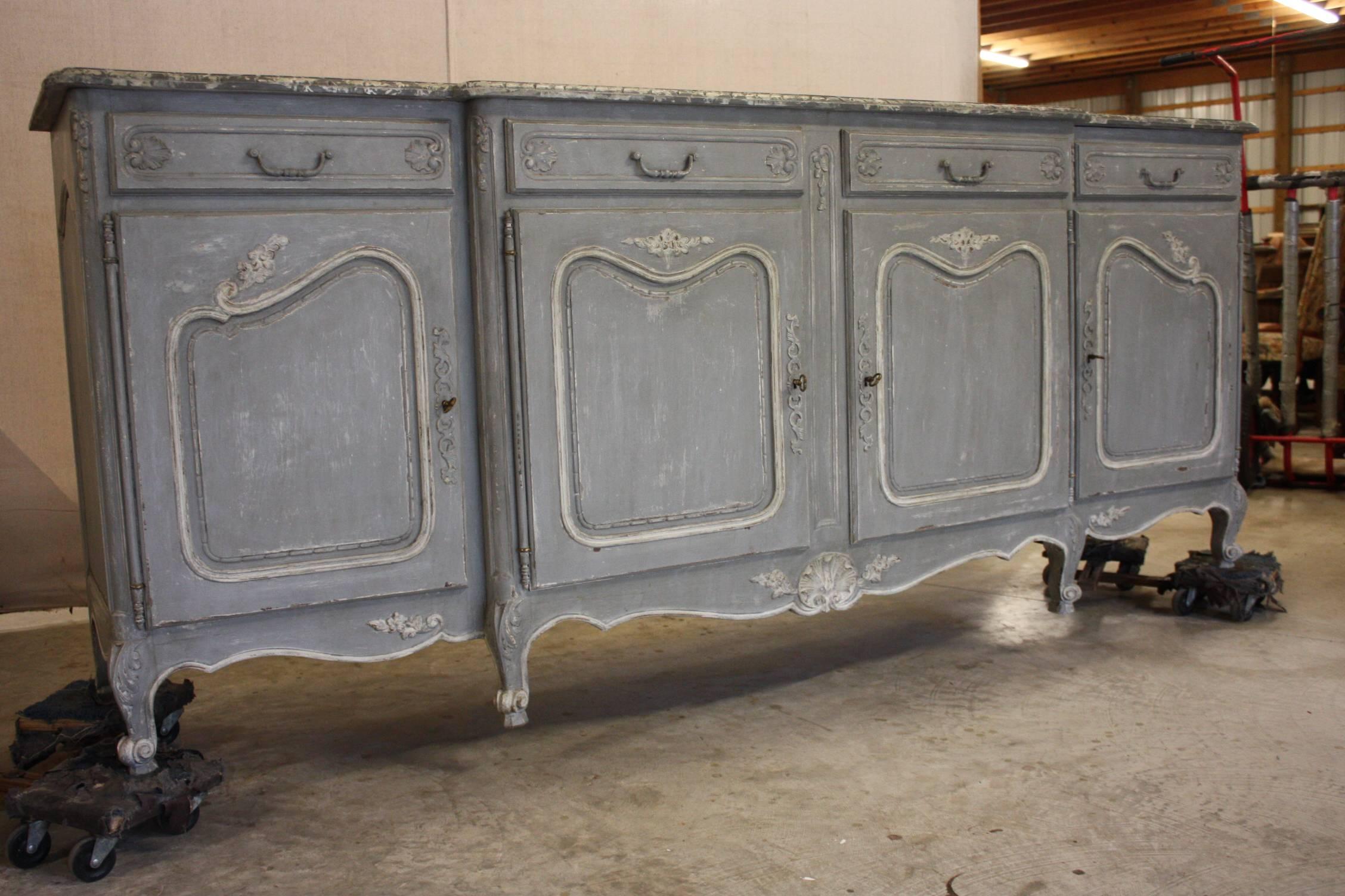 Painted French enfilade with faux marble top. Enfilade has four doors and four drawers with original hardware. Hand carvings on the doors, drawers and on the bottom of the enfilade. It is painted a pale blue and white undertones while the faux
