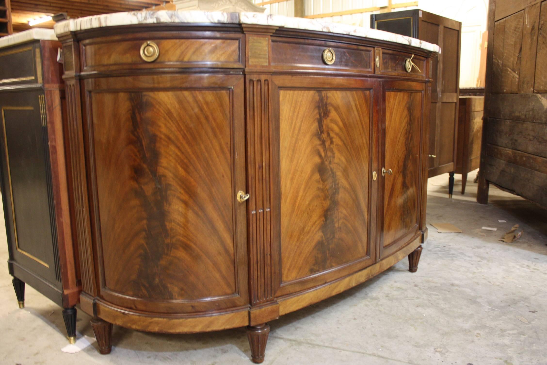 An extremely elegant French Louis XVI style buffet in mahogany.   ‘D’ shaped buffet is raised by circular fluted tapered legs.  Spectacular patina and a great piece that would add interest to any room.  