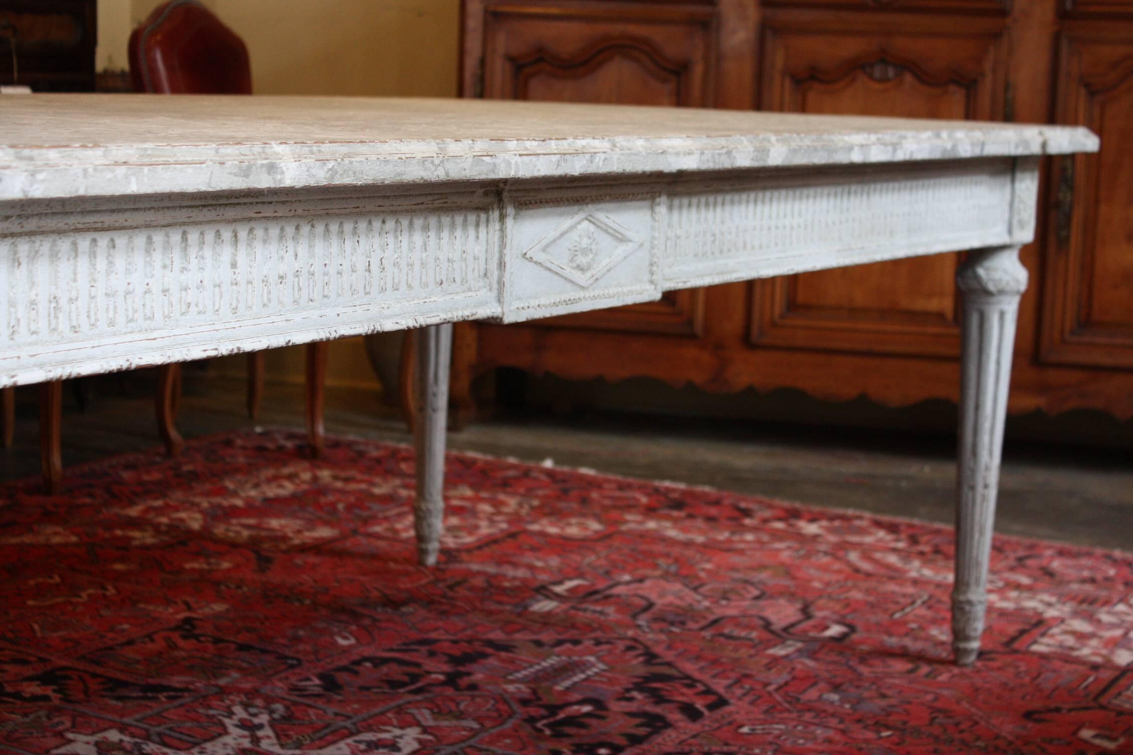 This is an exceptional antique Louis XVI painted dining room table crafted in northern France, circa 1860. The table has a faux marble top, a carved apron, tapered legs. The top is painted in a neutral gray palette with a faux marble design. This