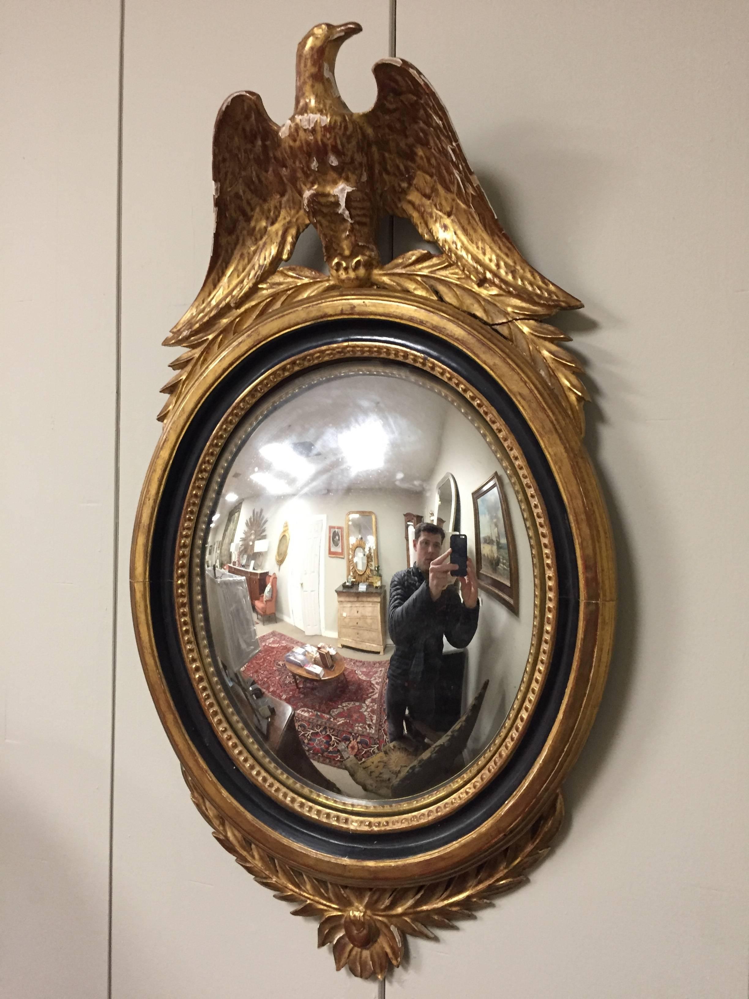 Late 19th or very early 20th century Regency carved and ebonized giltwood bullseye mirror. The convex mirror framed in a spectacular ebony and gilt decorated frame with a lower carving leading to an interior ebony frame. The top adorning a eagle