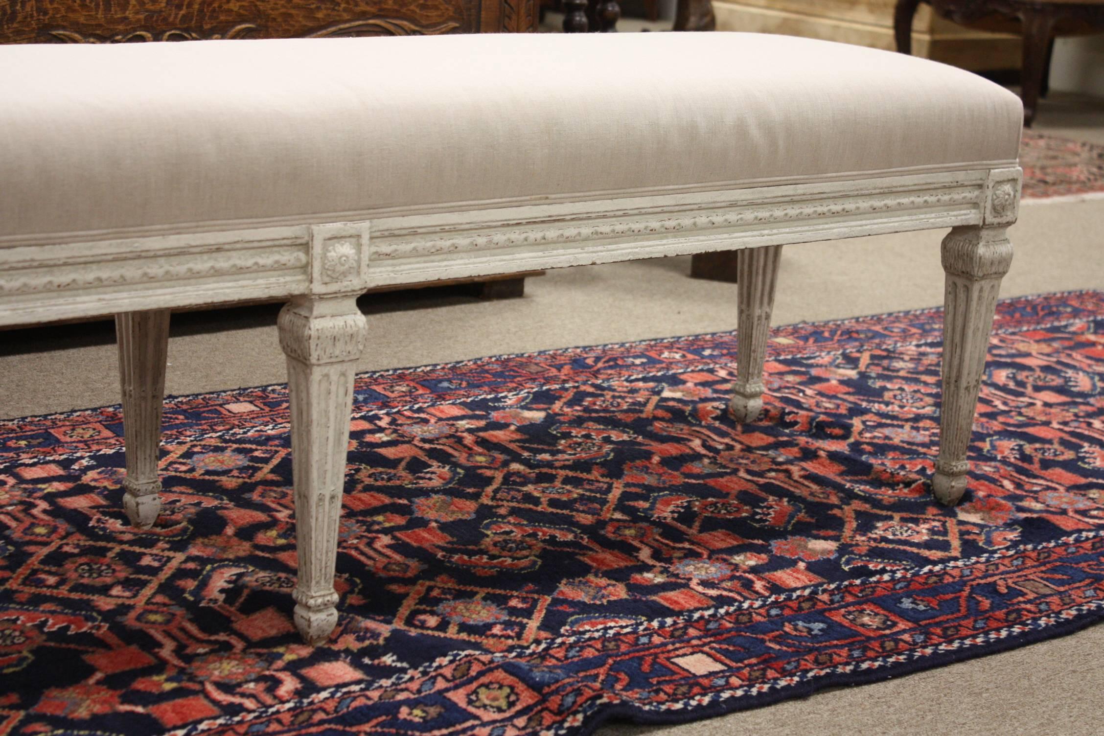 Louis XVI bench from France. Carved, circa 1880, the antique bench has six tapered legs, symmetrical carvings around the apron, and is reupholstered in a neutral. Due to its size and narrow profile, the bench would also make the perfect piece at the