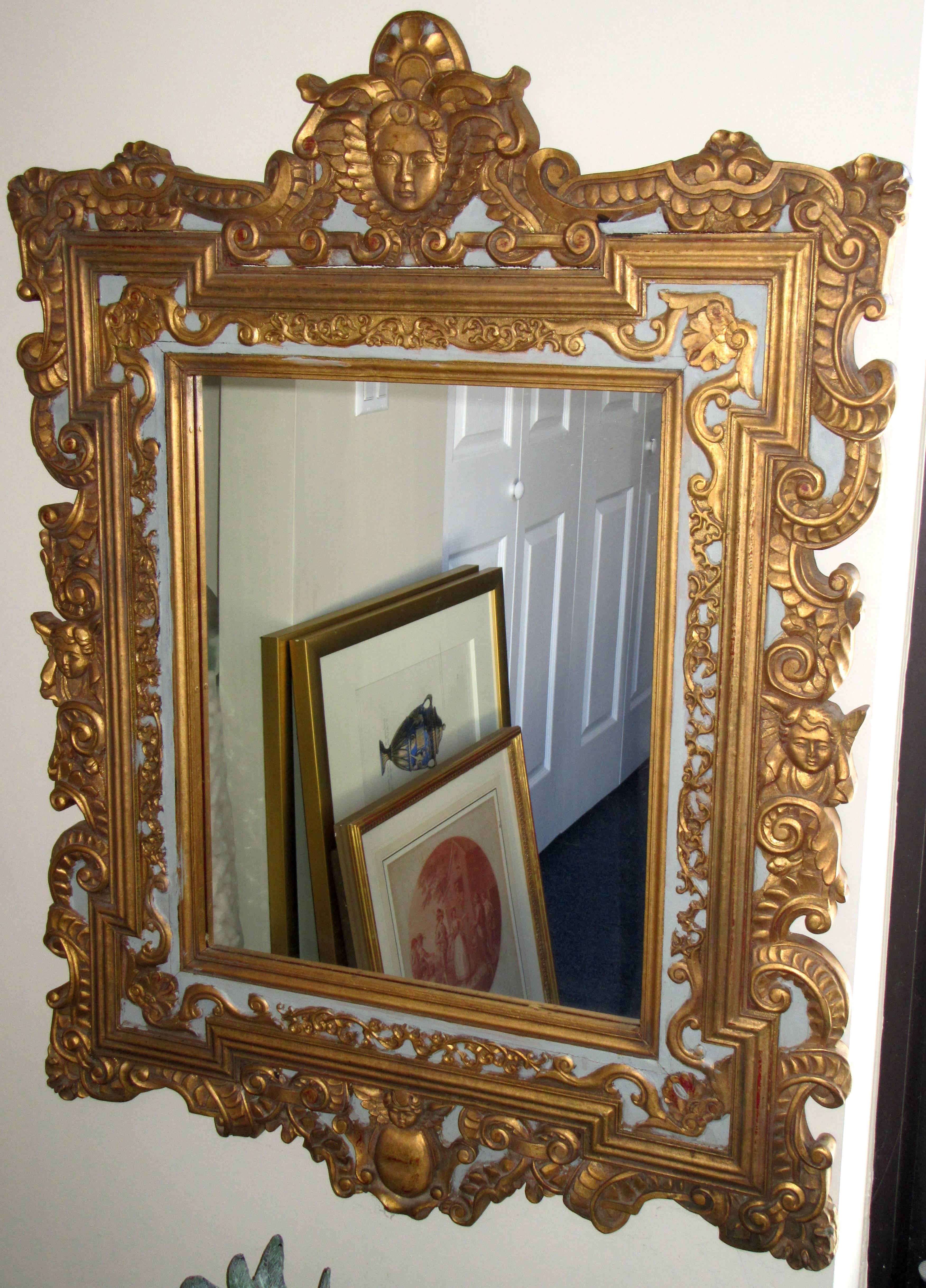 A pair of Baroque style carved and gilded wood wall mirrors. The background of the frame is painted in a pale blue.