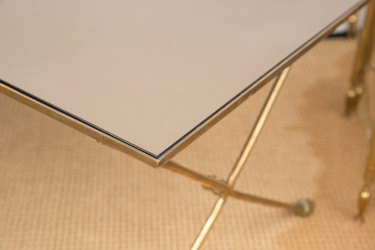 A low rectangular brass cocktail/coffee table with a mirrored glass top. The slim 
