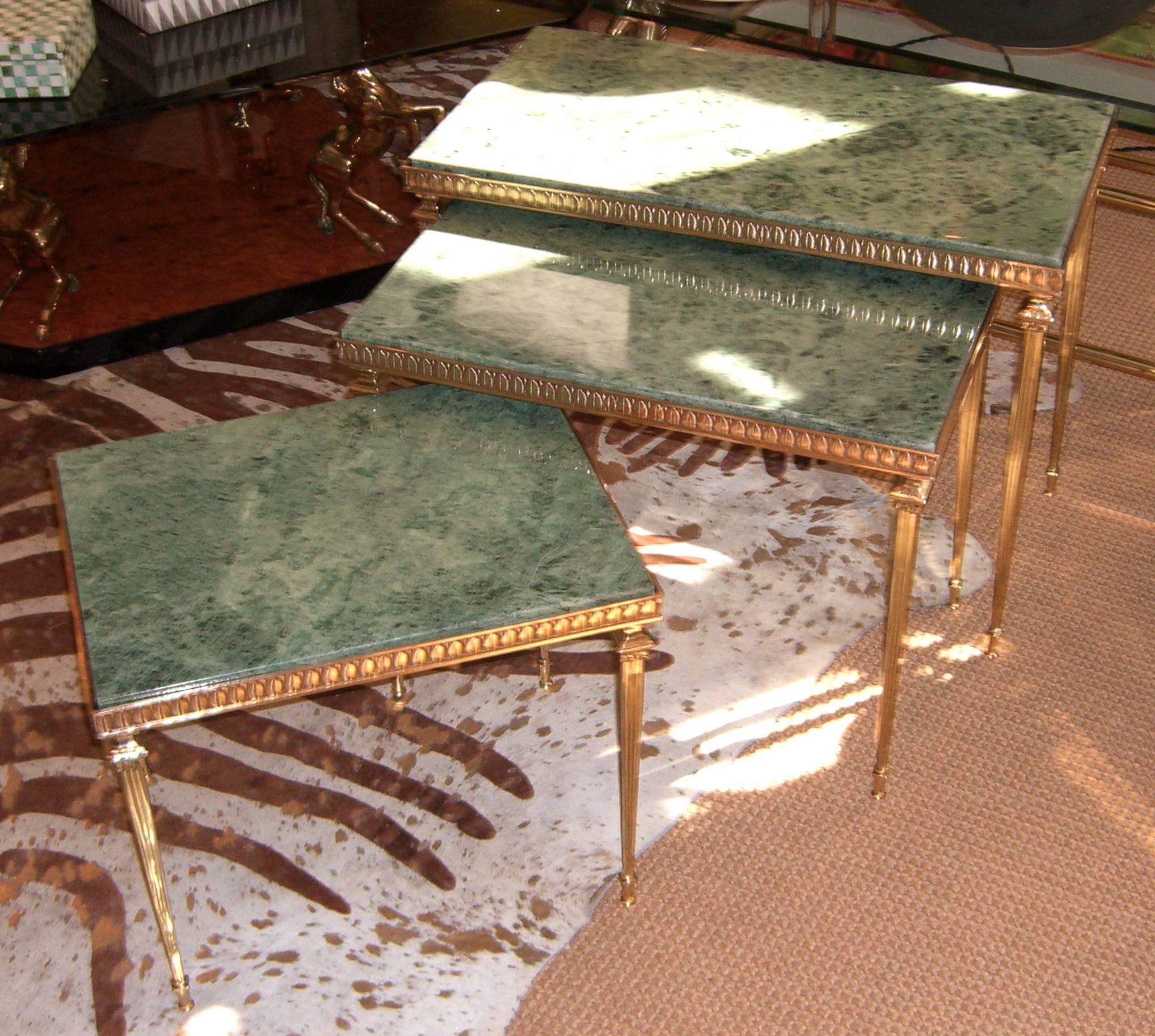 A group of three rectangular nesting tables. The bases are polished and lacquered brass with a delicate leaf design and decorative neoclassic style legs. All tops are inset green marble with deeply shaded veining.