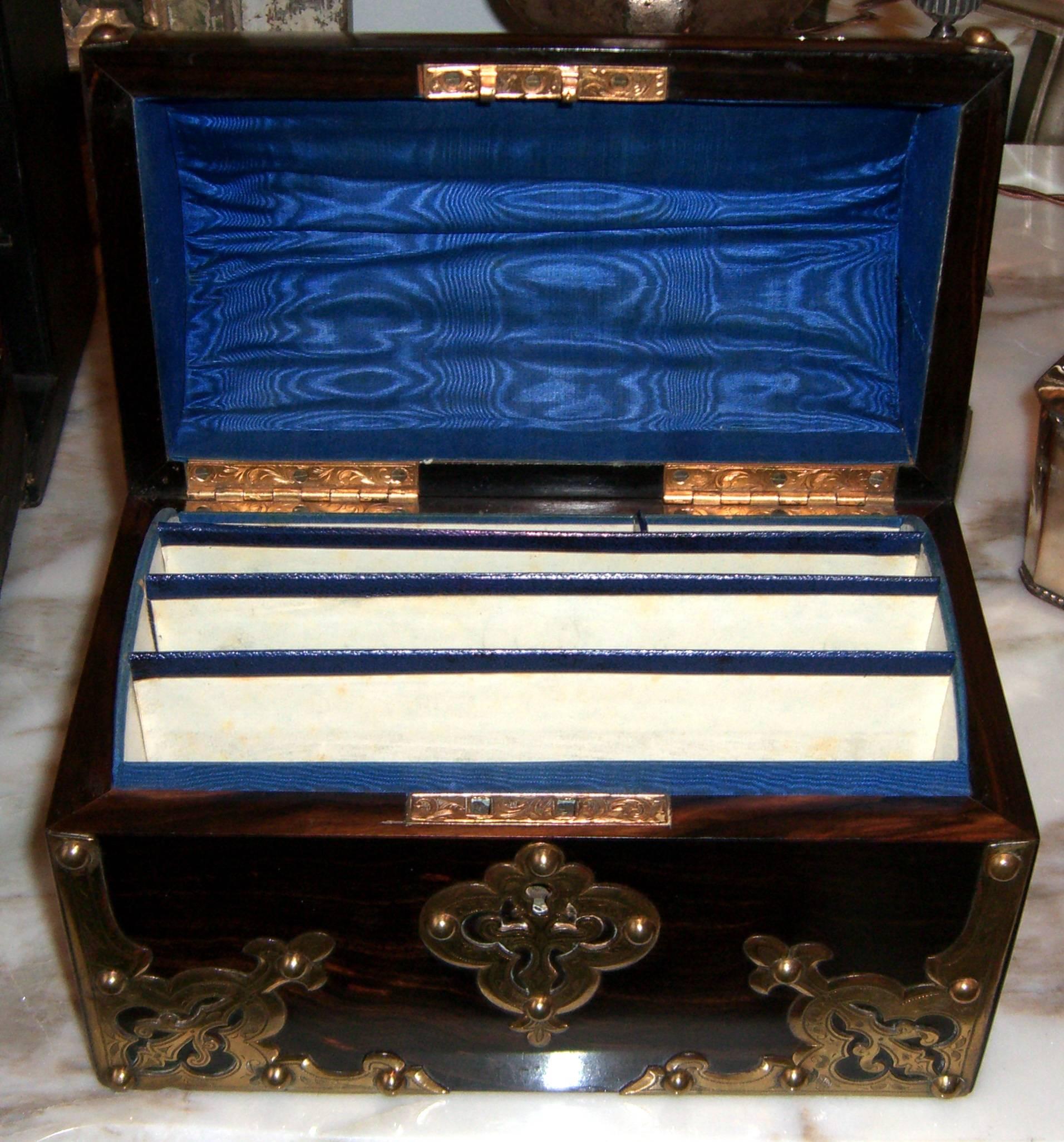 A very attractive Victorian coromandel veneer box. It is of domed top form in the traditional treasure chest shape and is clad with decorative brass mounts and hinges. The interior has five heavy paper compartments trimmed in blue leather. The top