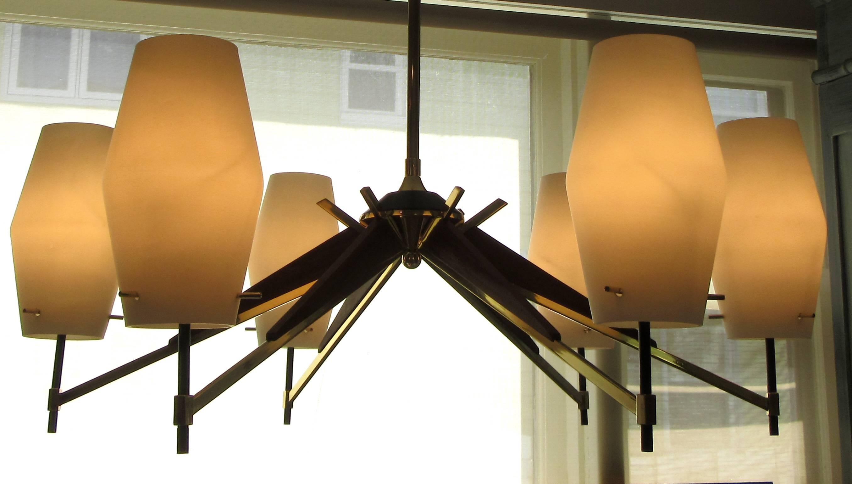 A large six-light Danish modern chandelier. Six arms of walnut and brass terminate with an opaque white glass cylinder form shade. The chandelier hangs from a brass rod. The sockets hold candelabra size bulbs. Pictured when lit is with 25 watt bulbs