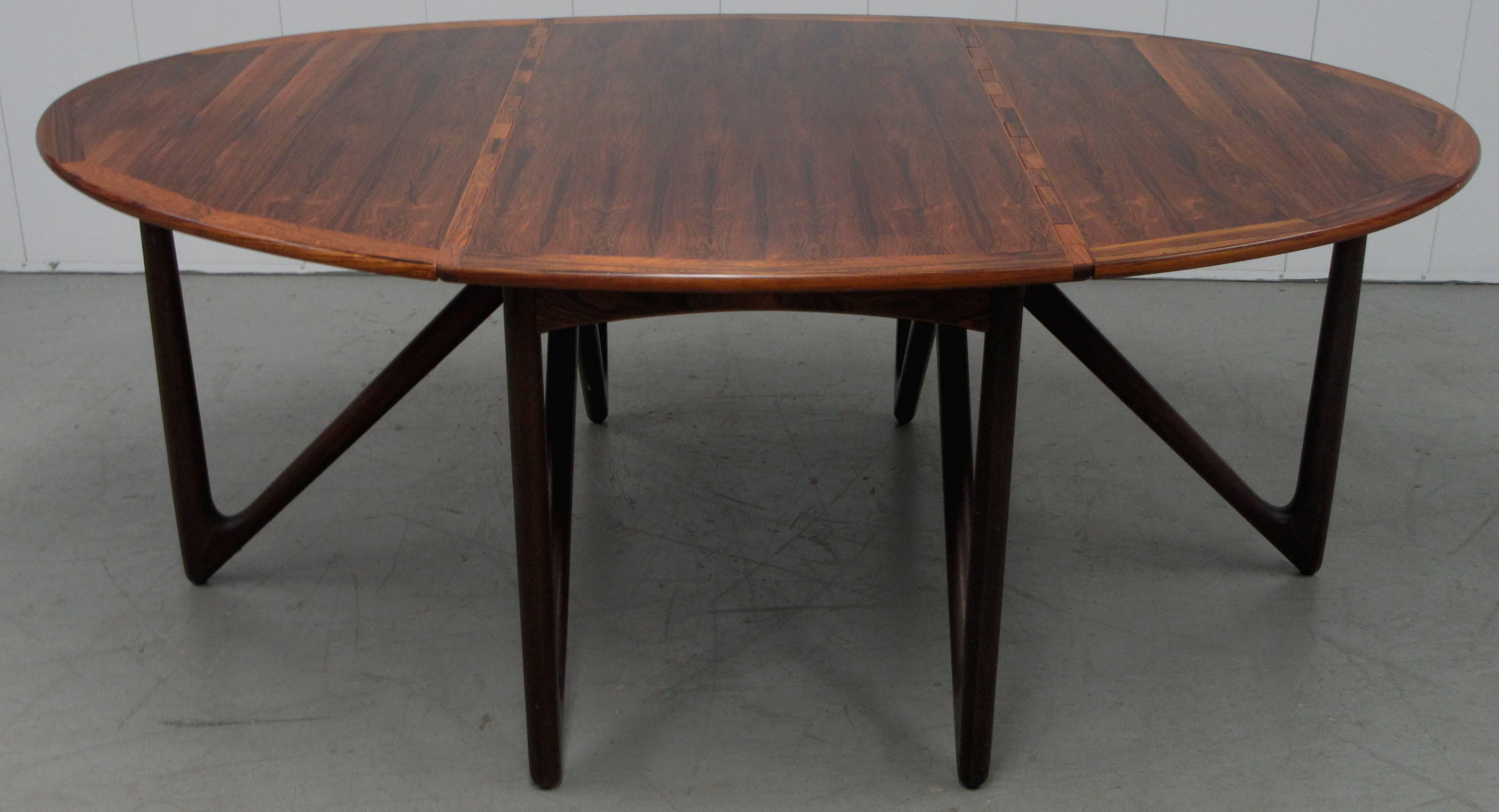 A solid rosewood Danish Modern gateleg dining table. When extended the dining table is oval. The ends drop down on knuckle hinges to be used as a rectangular console. The table includes custom-made pads. (pictured)
The measurements when the leaves