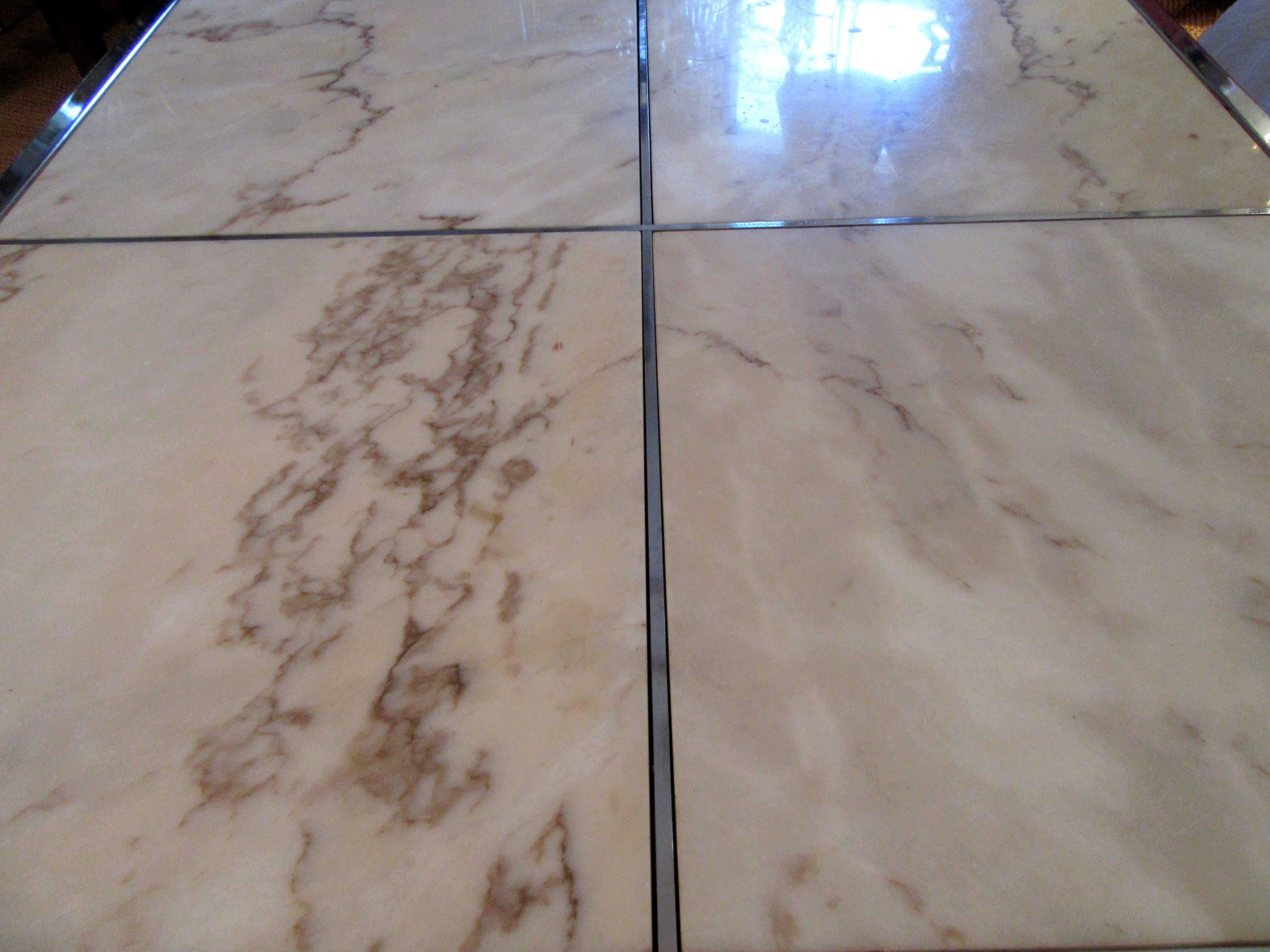 A square coffee or cocktail table with a base of rectangular chrome. The top is divided into four sections, each of which has inset Portuguese marble.