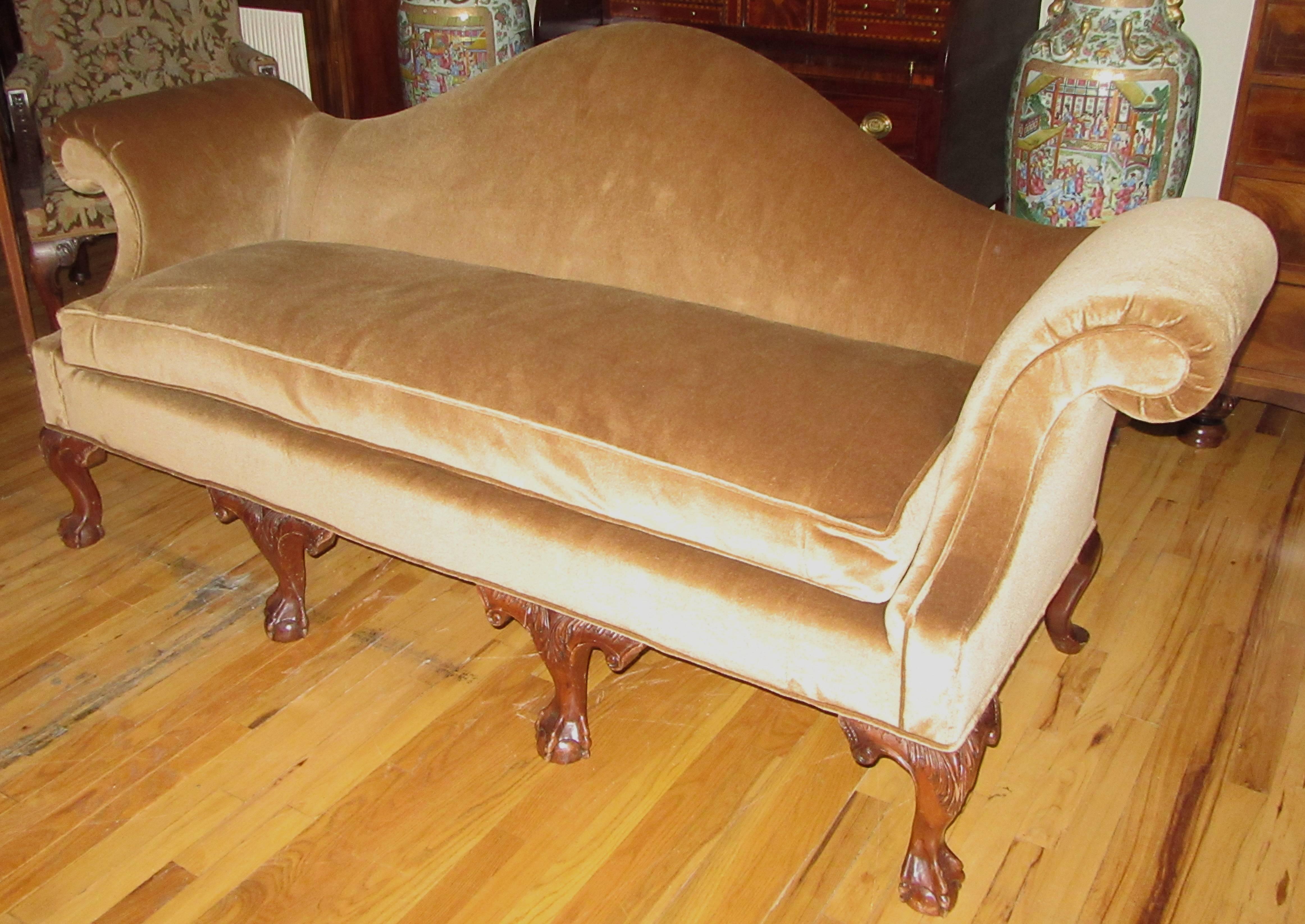 A long camelback sofa on eight cabriole mahogany legs. The front are hand-carved acanthus leaf and scroll design terminating in claw and ball feet. Newly upholstered in a golden velvet silk mohair with a single down filled cushion.
