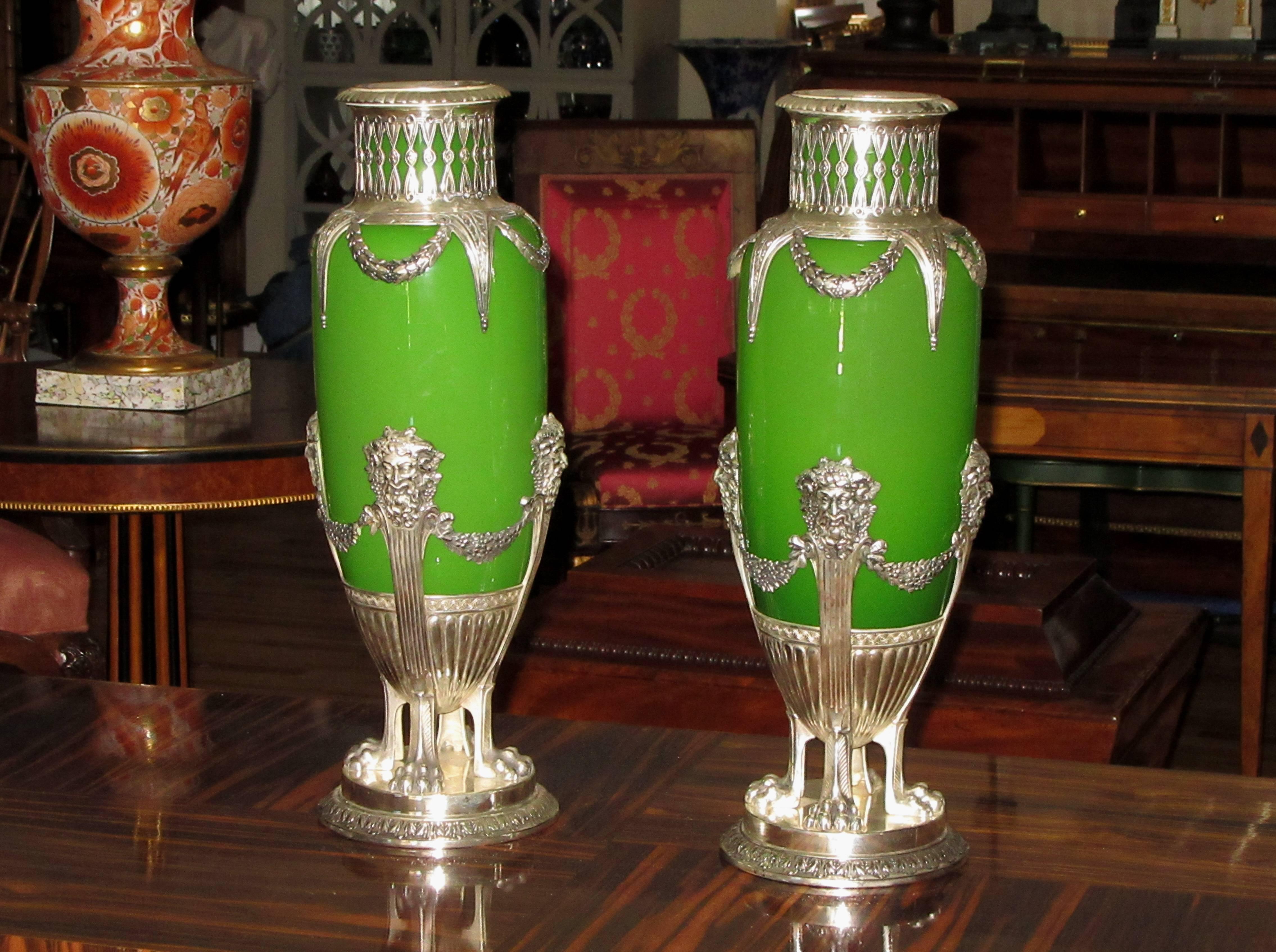 A pair of ovoid shaped vases in green opaline glass held in silvered metal mounts. Each vase is crowned with an openwork gallery that descends to the body of the vase in the form of draped laurel garlands. The body of each vase rests in a round base