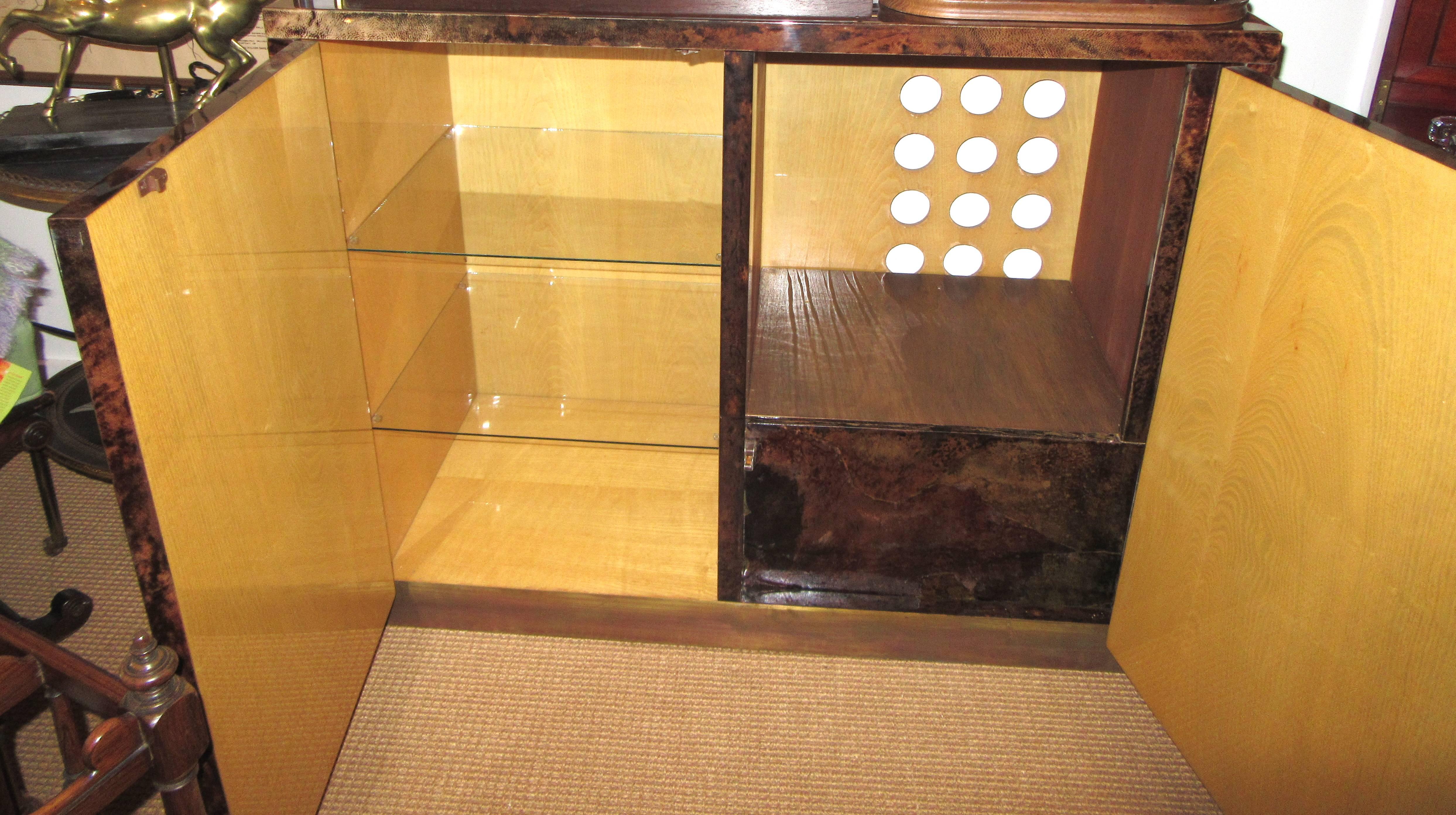 A brown high shine lacquered parchment two sided cabinet. The push to open doors reveal double glass shelving on the left, and on the right space for a dry bar or media equipment. The original cabinet held a vintage 