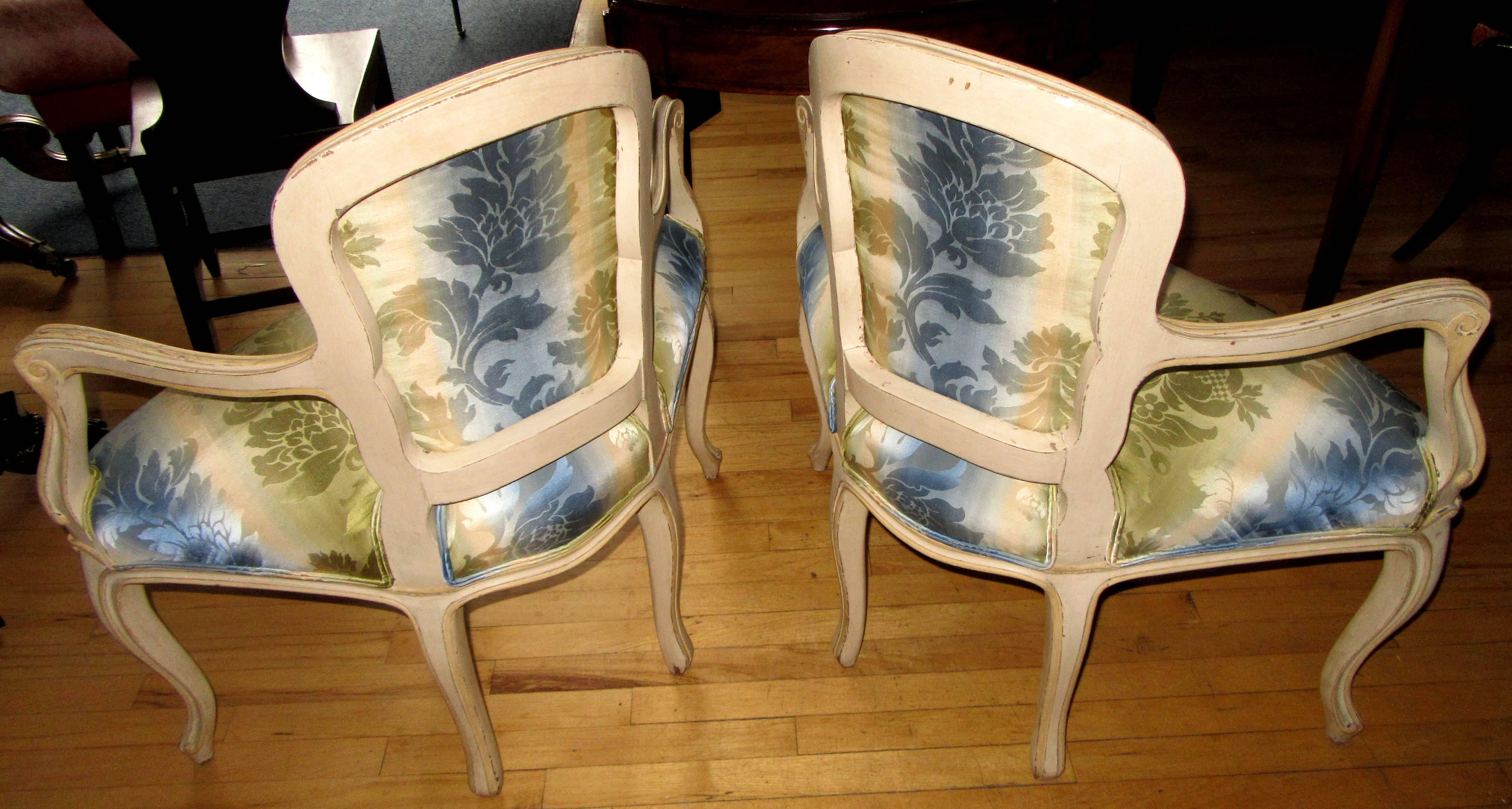 A pair of Louis XV style cream painted corner chairs each with cartouche shaped padded backs and seats on cabriole legs terminating in scrolled feet.