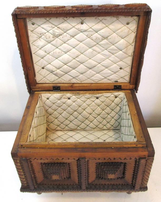 A handcrafted Tramp Art box or small chest. A detailed design on four tapered feet. The interior is lined with white quilted fabric and the lid is fitted with a large finial. The bottom is signed.