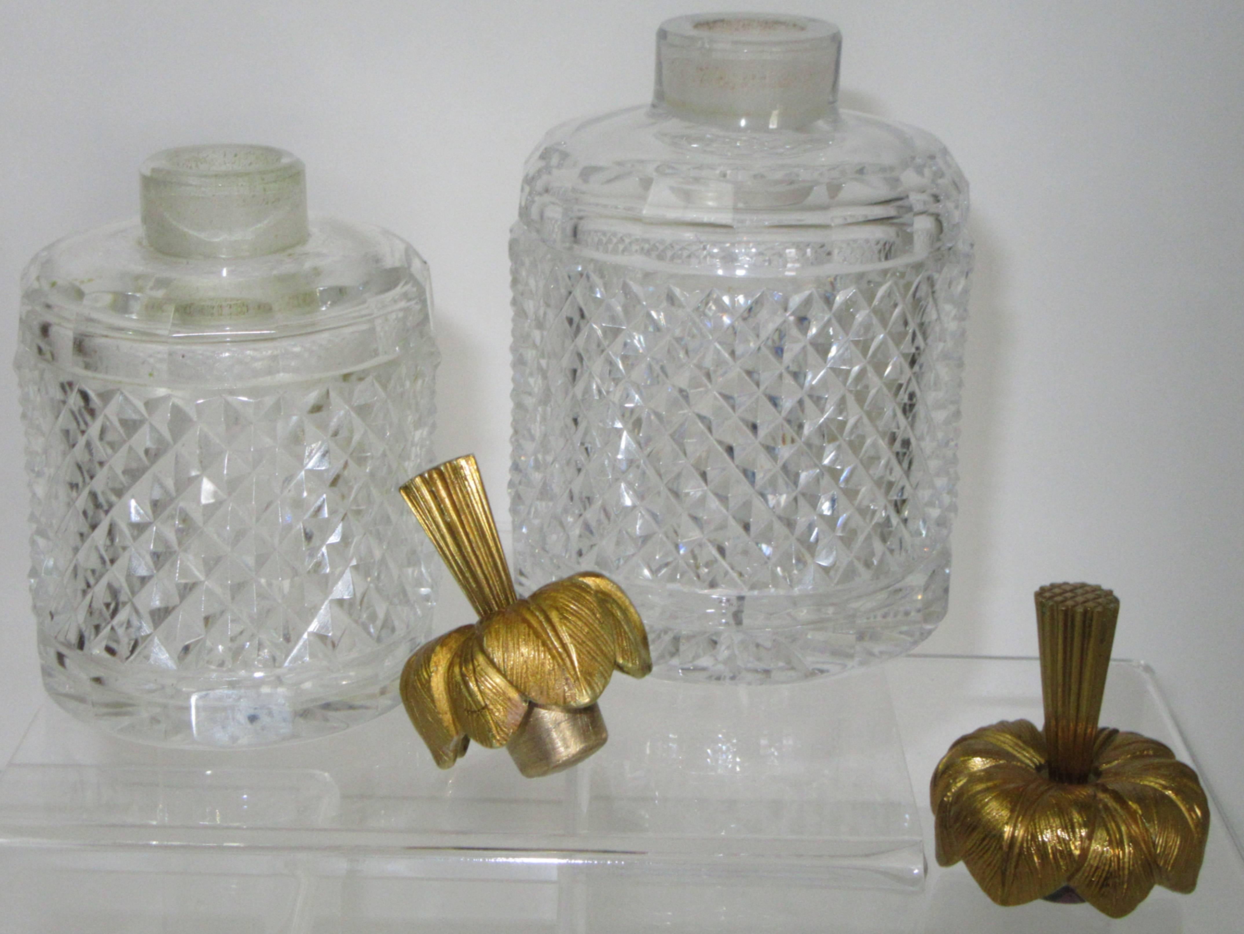 A large and a small, two round crystal bottles with bronze doré flower form stoppers.