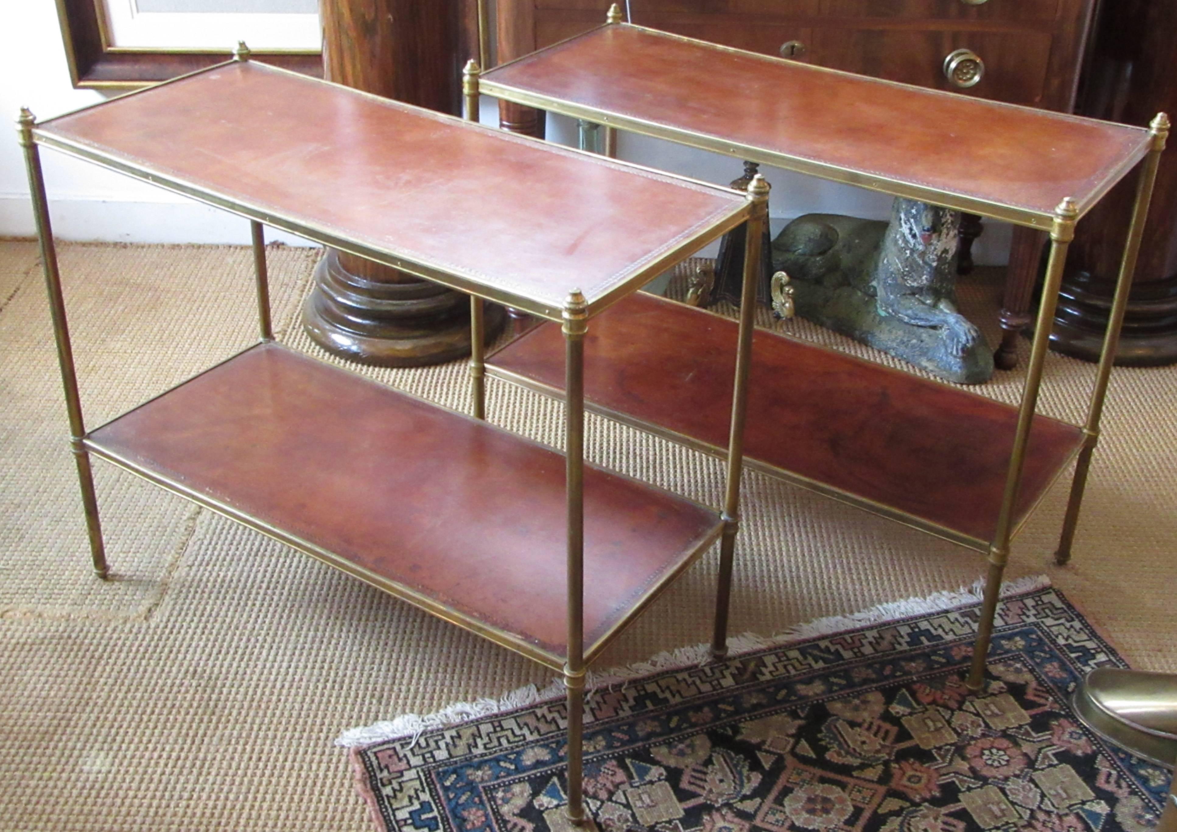 A pair of rectangular brass end tables with brown embossed leather shelves.