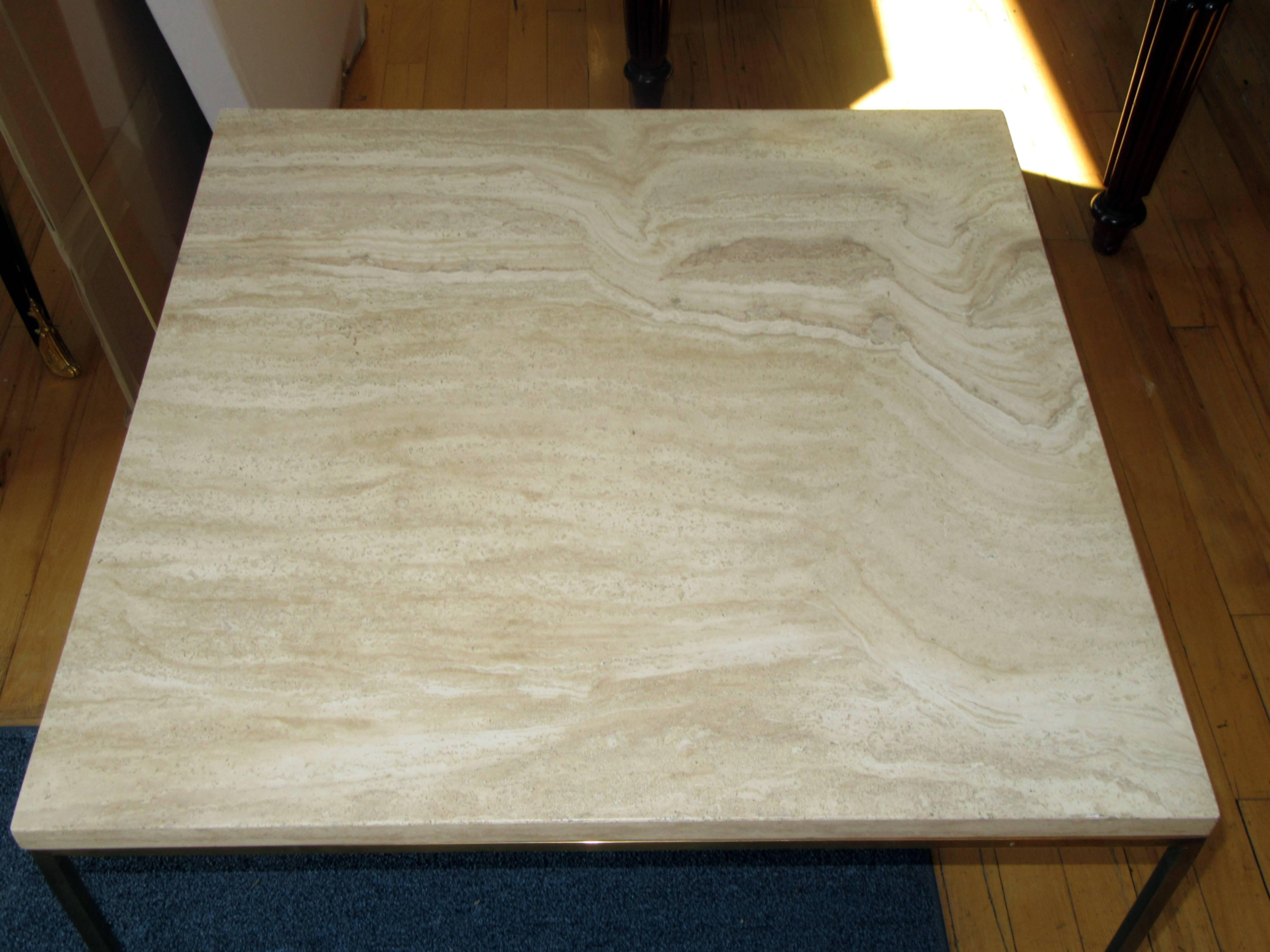 A square coffee or cocktail table with a solid travertine top on a simple brass base.