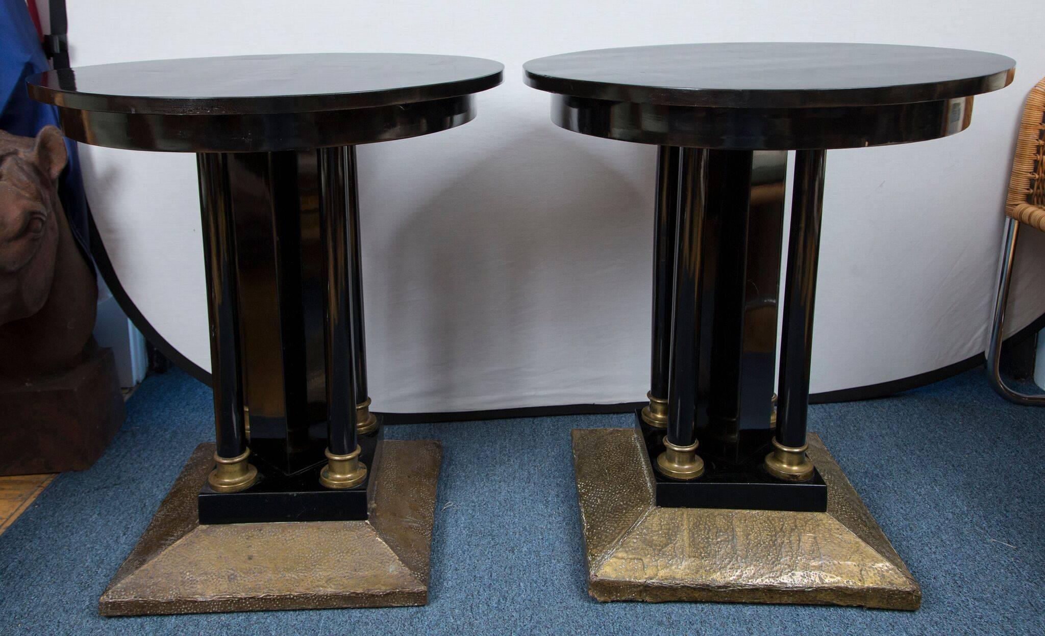 A pair of black lacquered wood tables with pedestal bases. The square foot of each base is mounted in hand-hammered brass and the pedestal columns sit in brass caps.