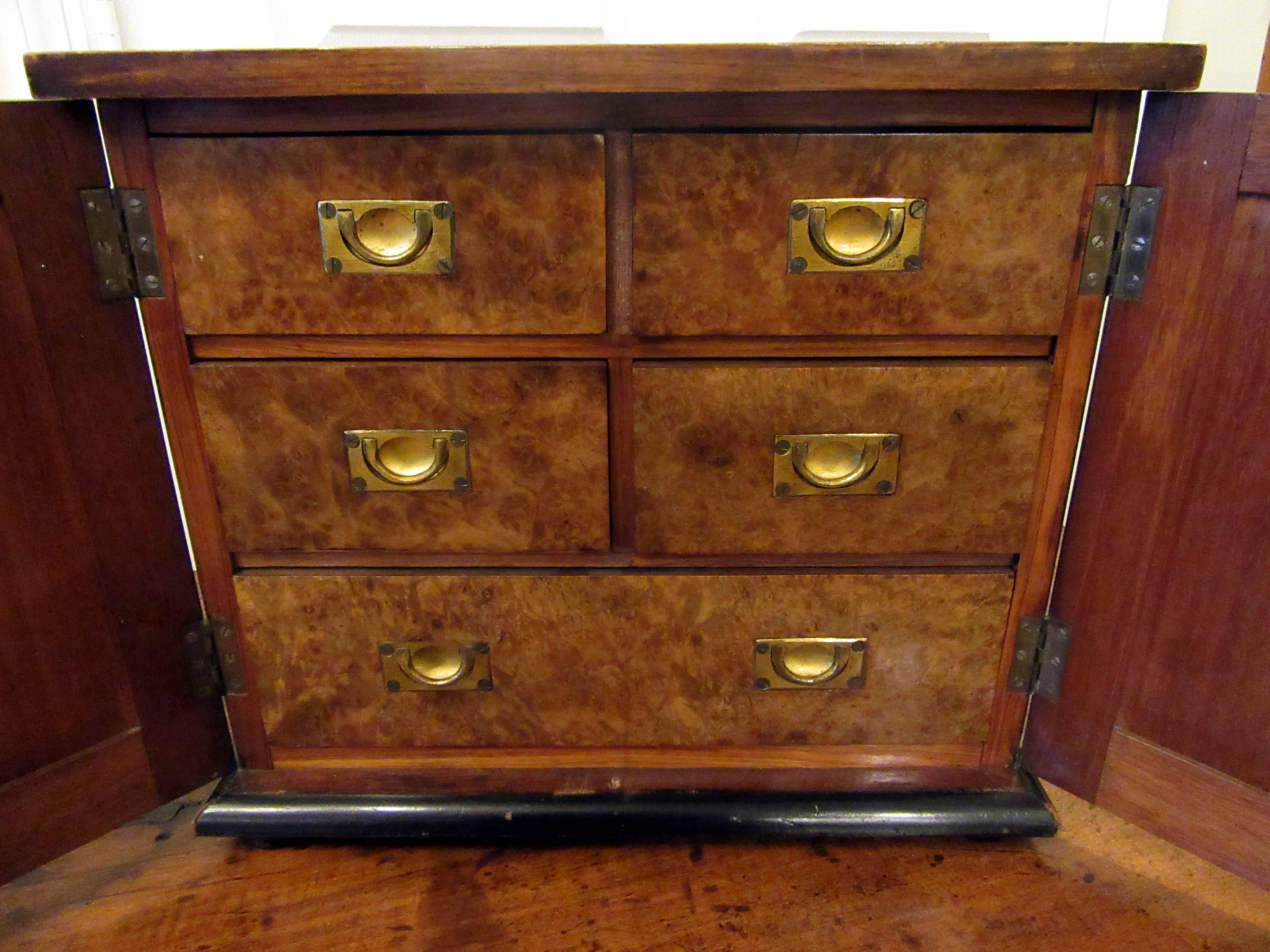 A small chest of five drawers with brass pulls behind paneled doors.