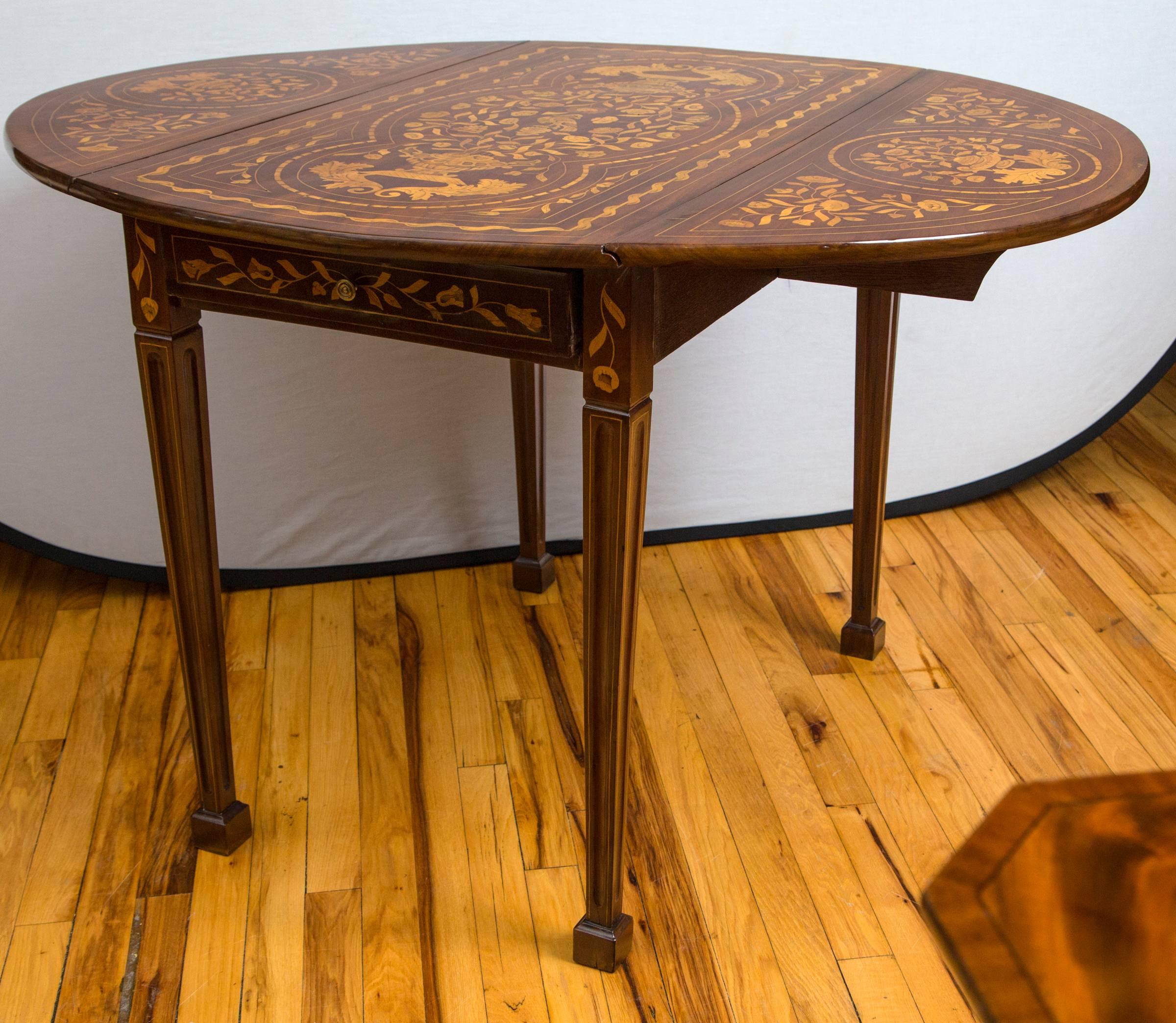 An extensively satinwood inlaid walnut drop-leaf table with tapered legs terminating in spade feet. I single long drawer opens on either end. When leaves are up the table is an oval of 46.5 inches in width. Measurements listed are at the leaves