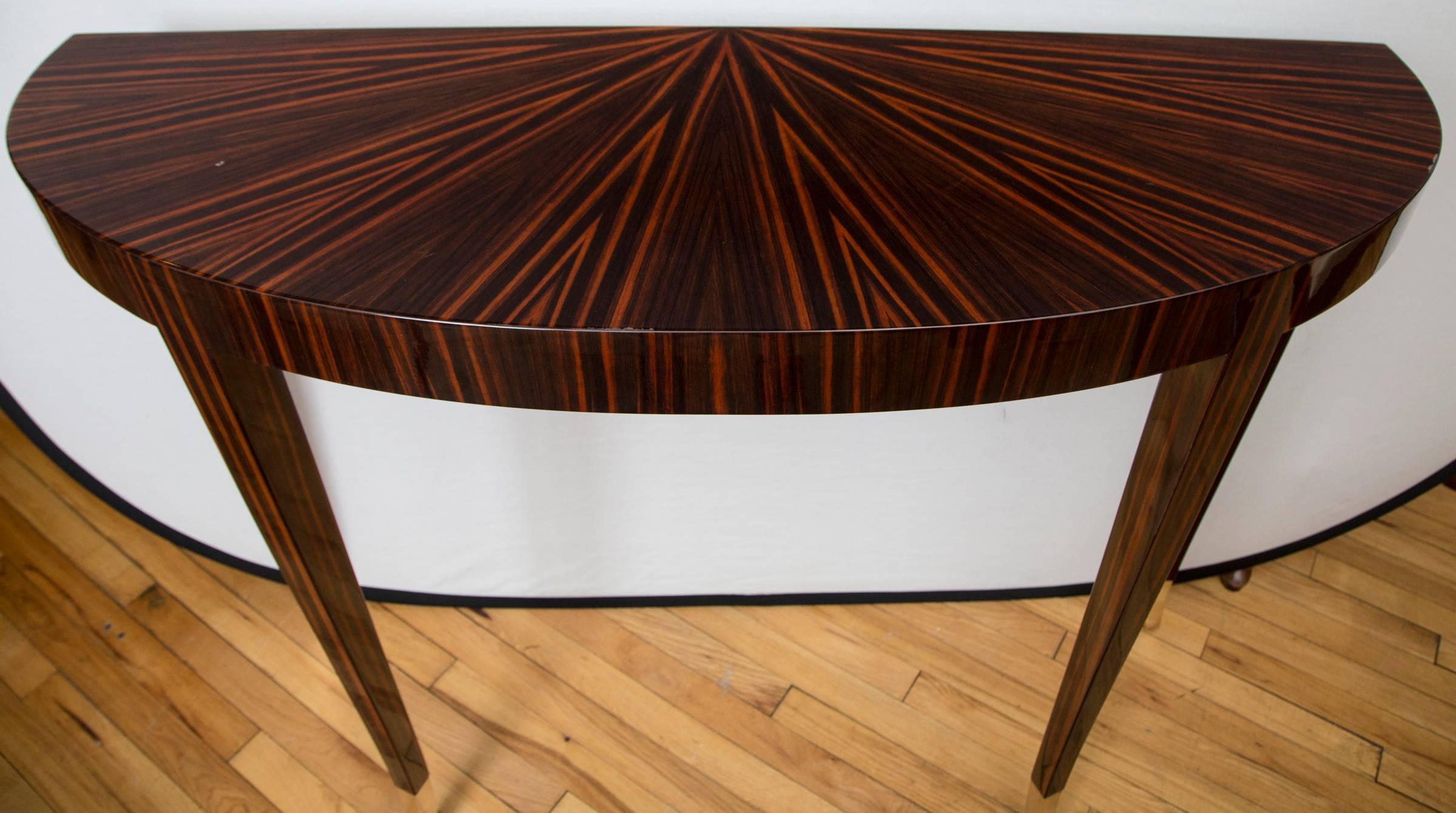 A pair of Macassar ebony veneer, high polish lacquered demilune consoles. Tall, tapered legs are fitted with brass sabots.