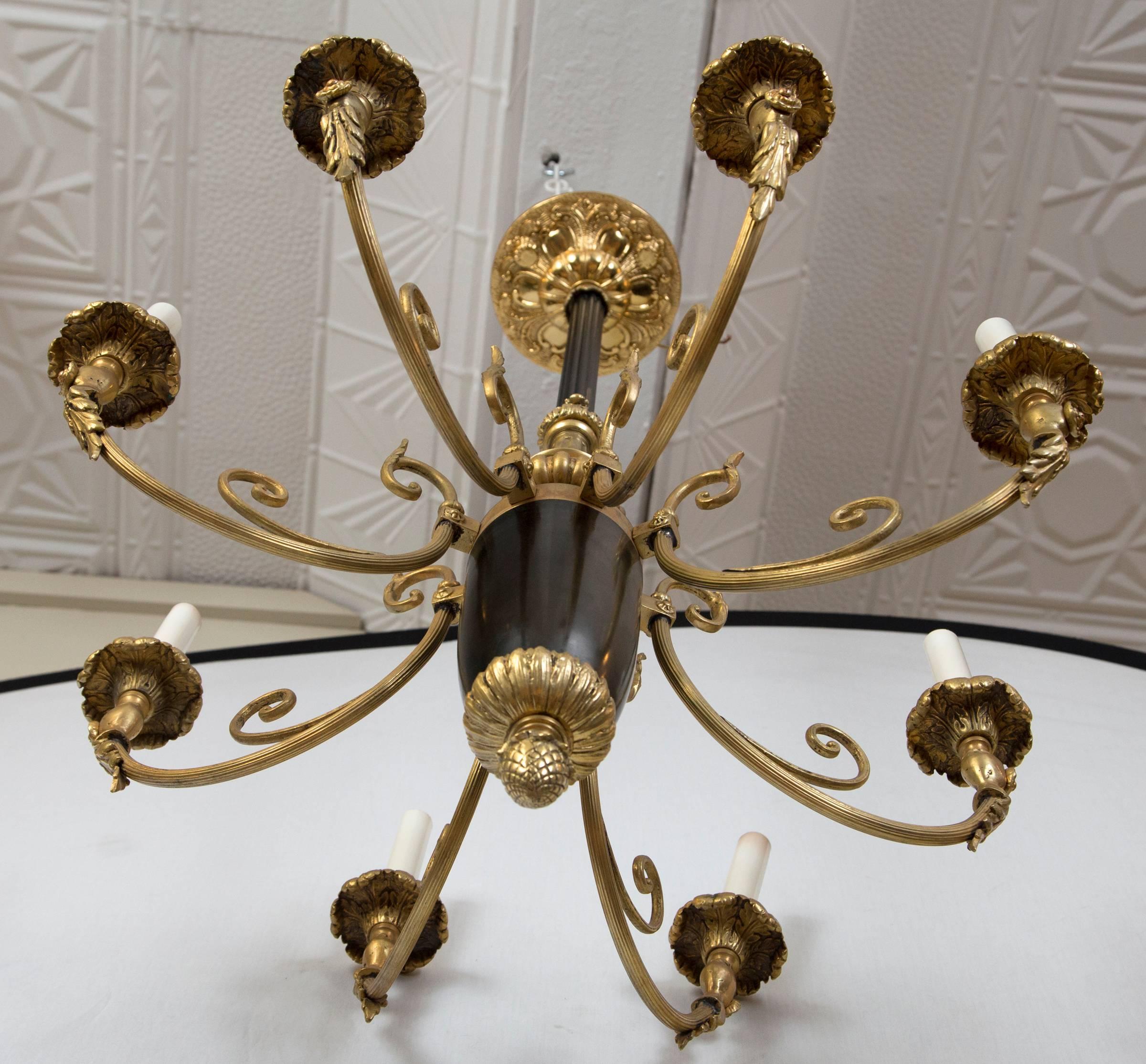 Gilt bronze and black tole eight-light chandelier. Eight long upturned arms with foliate decoration. The tole centre terminates in a large acorn finial. A ceiling canopy is included.