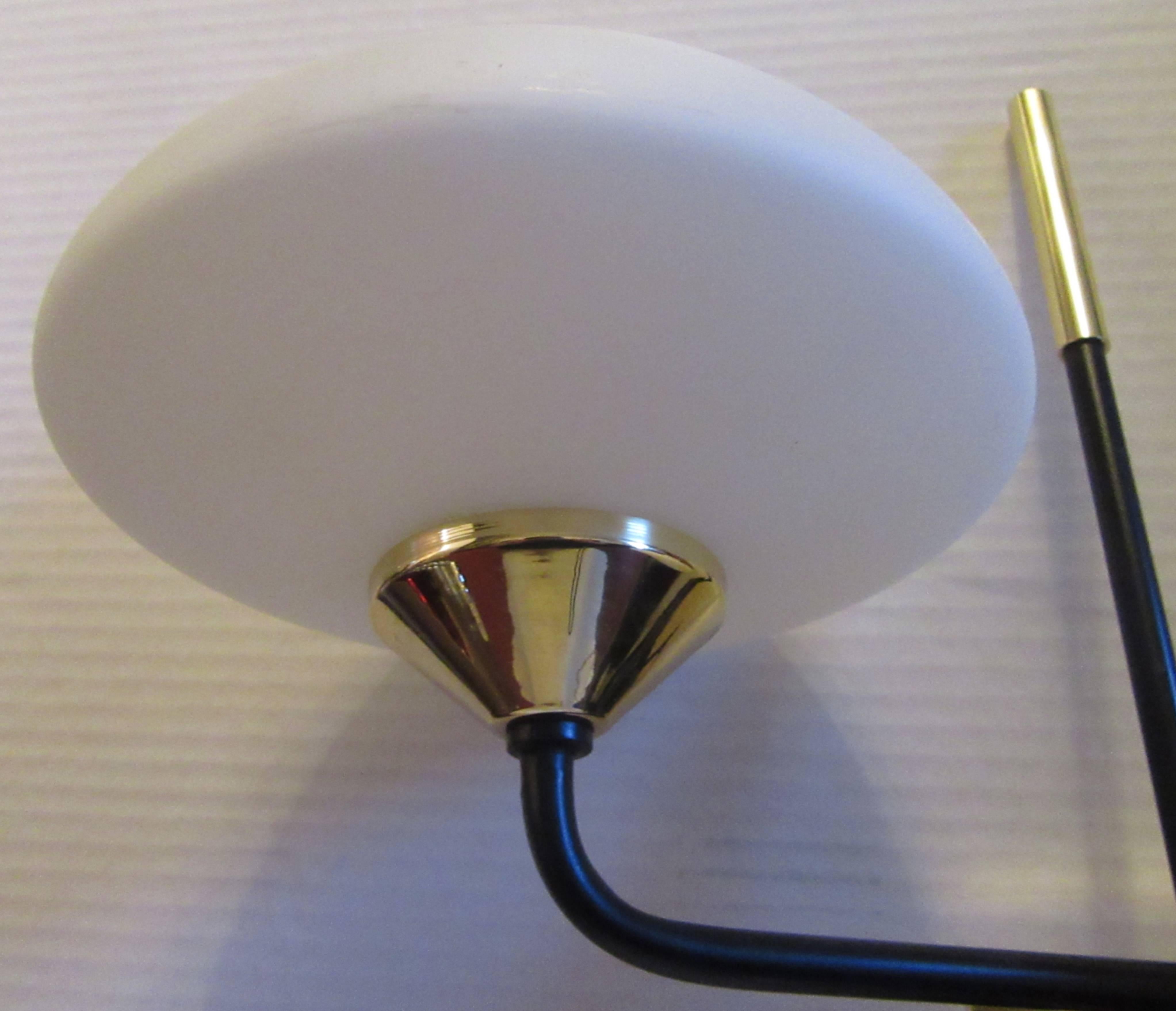 Simple and sleek brass and black metal wall lights with opaque white saucer form globe lights. All newly wired for the U.S., and a new brass backplate has been added for modern electrical.