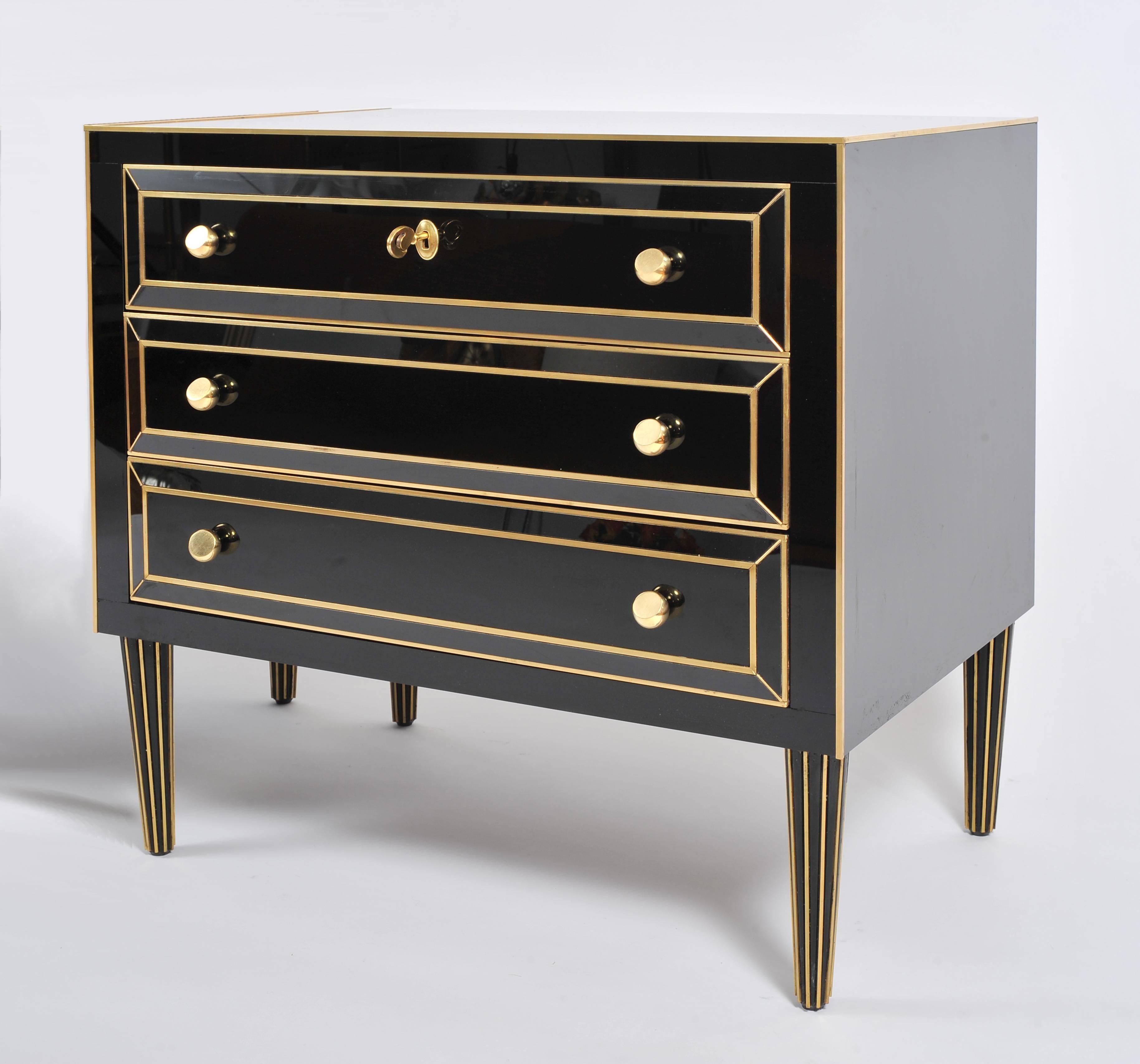 Well-proportioned pair of Italian three-drawer black glass chest-of-drawers. Each piece features brass detailing throughout, tapered black and brass legs and brass half ball handles. Original keys. The interior of the drawers are lined in felt with