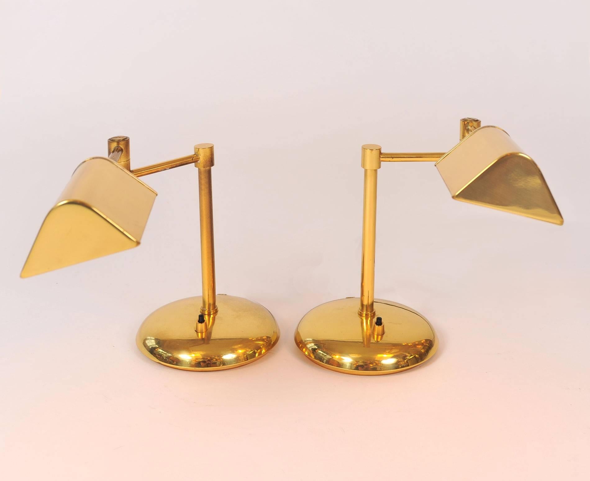 Pair of brass table lamps, each with rotating arm that adjusts lamp position and lampshade handle that adjusts shade position. Circular curved base holds the switch.